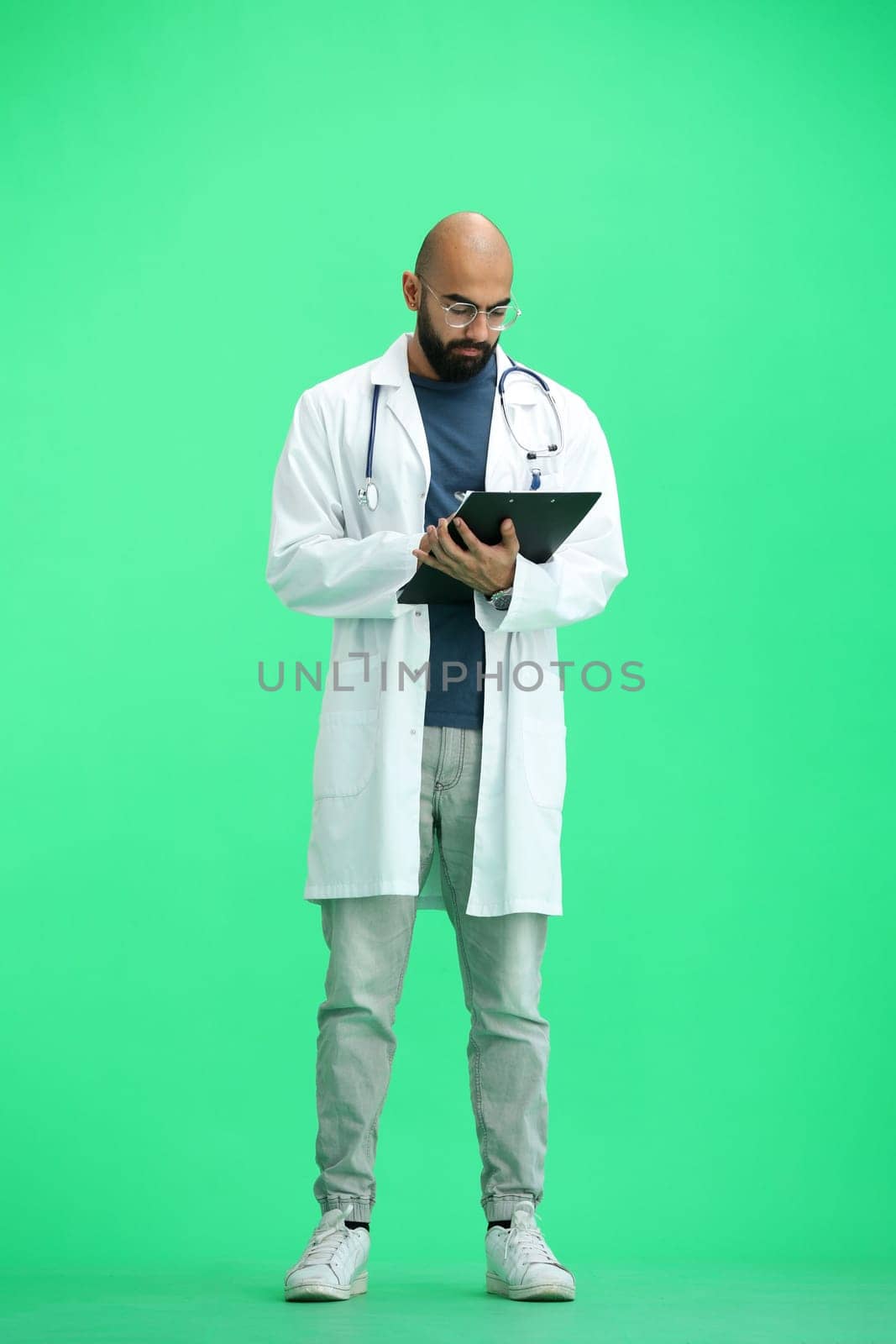 A male doctor, on a green background, in full height, writes.
