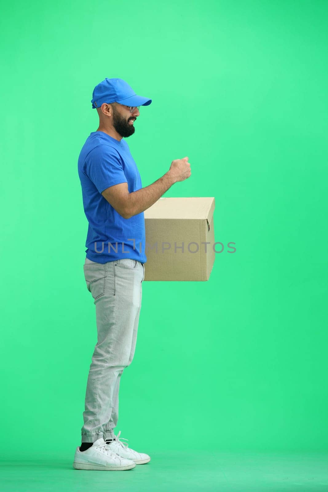 A male deliveryman, on a green background, in full height, with a box, shows a stop sign.