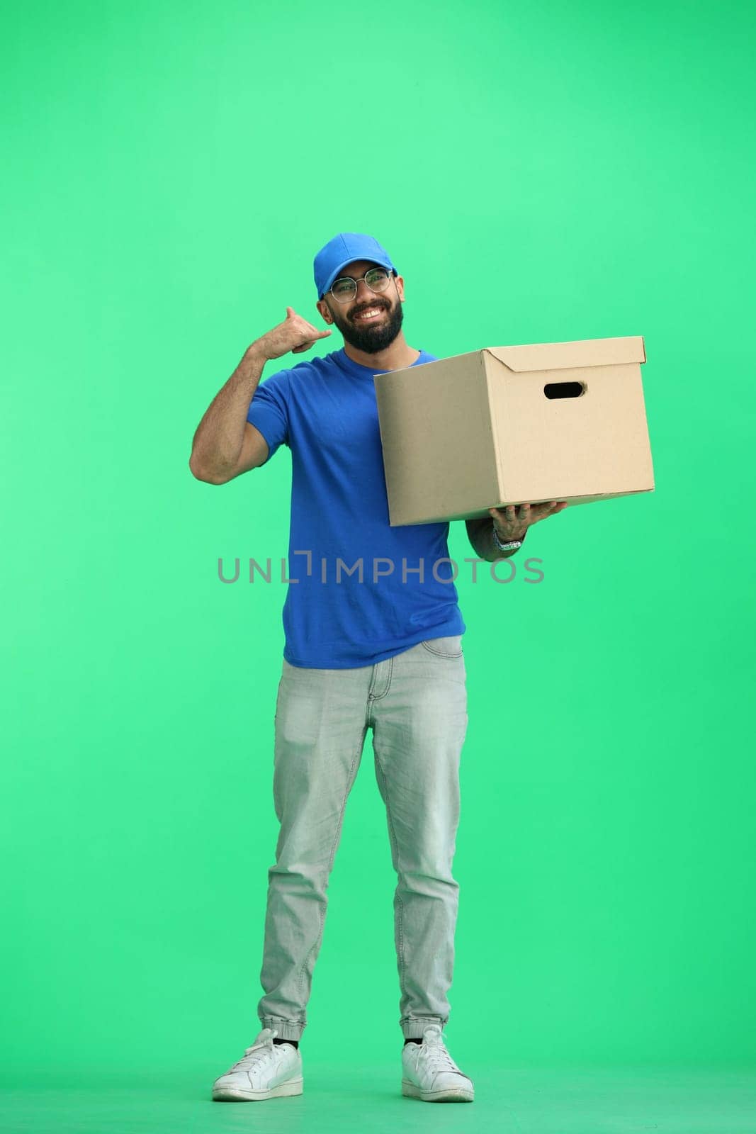 A male deliveryman, on a green background, in full height, with a box, shows a call sign by Prosto