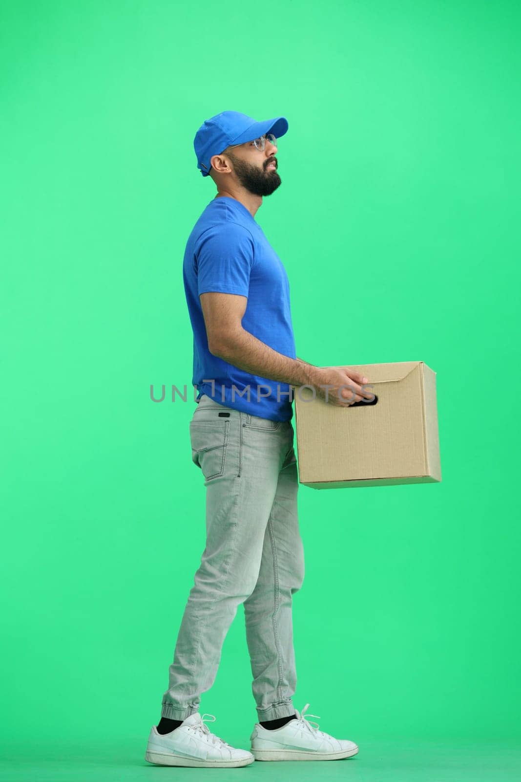 A male deliveryman, on a green background, full-length, with a box.