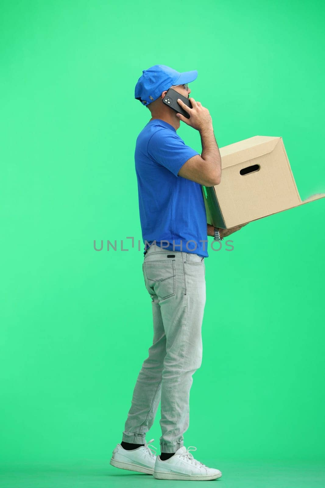 A male deliveryman, on a green background, in full height, with a box and a phone by Prosto