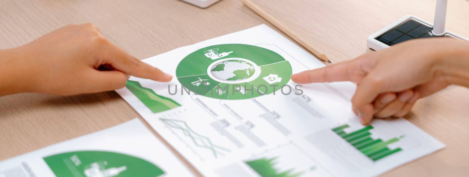 Rising graph representing the profit of using clean energy, displayed on a table at a green business meeting. Environmental documents was scattered around the table. Closeup. Delineation.