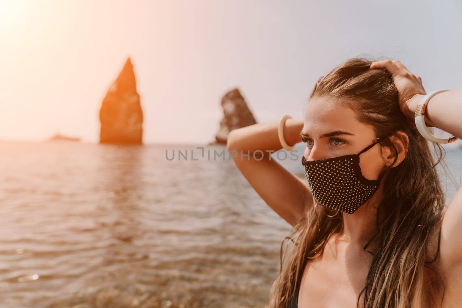 Woman summer travel sea. Happy tourist in black mask enjoy taking picture outdoors for memories. Woman traveler posing on the beach at sea surrounded by volcanic mountains, sharing travel adventure by panophotograph