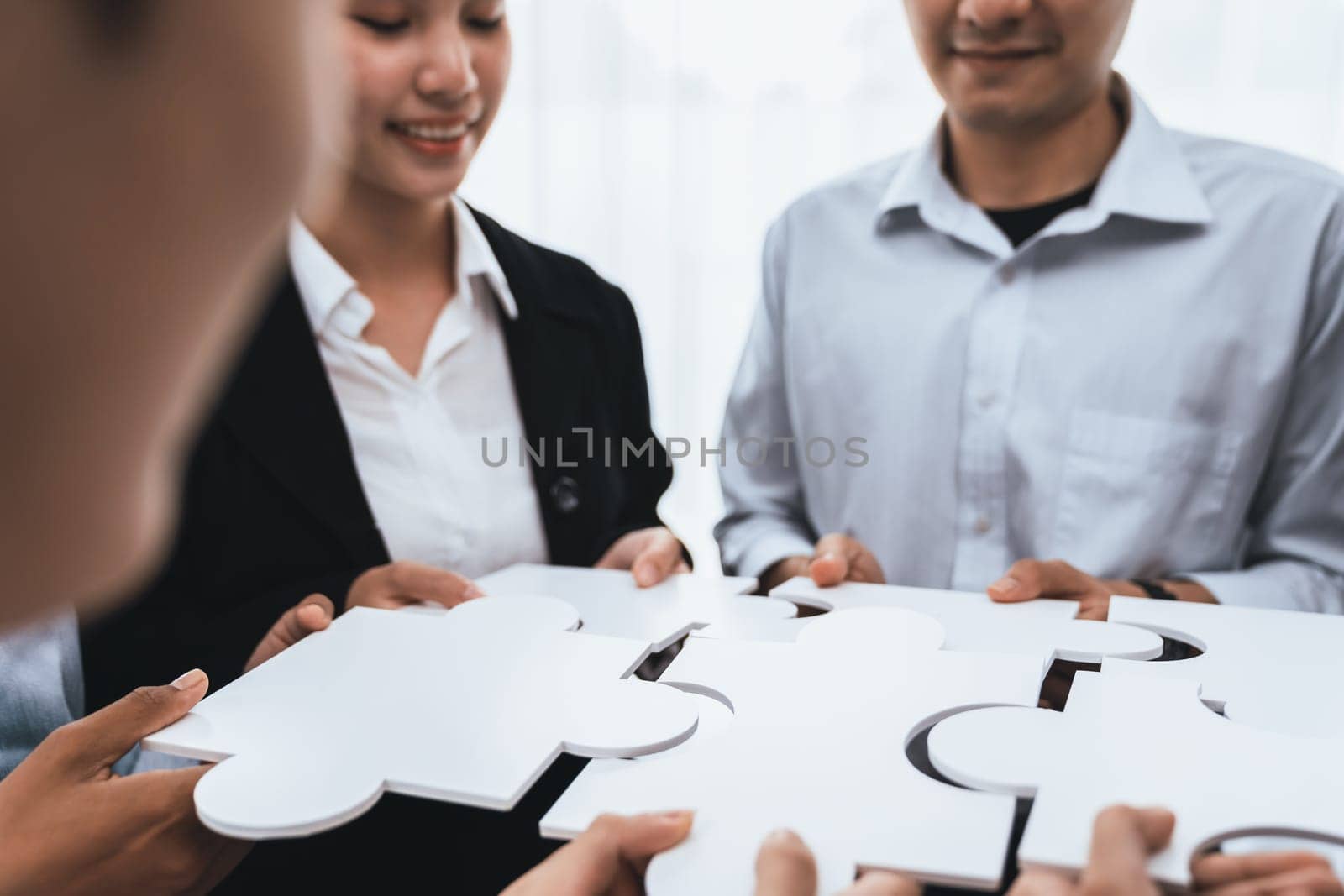 Diverse corporate officer workers collaborate in office, connecting puzzle pieces to represent partnership and teamwork. Unity and synergy in business concept by merging jigsaw puzzle. Concord