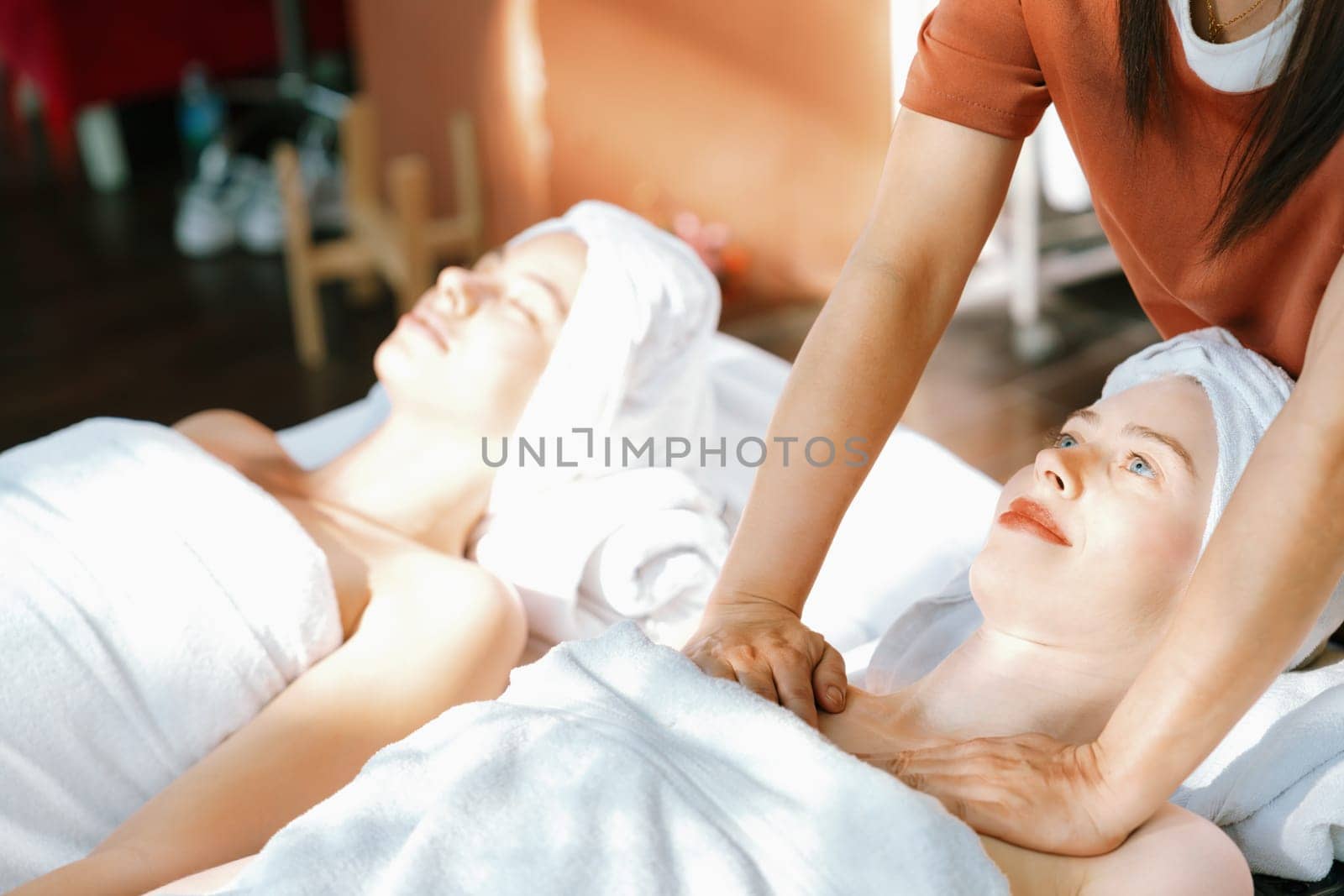 A portrait of two beautiful woman having back massage by professional masseur and falling in deep relaxation surrounded by traditional spa environment. Calming and relaxing concept. Tranquility.