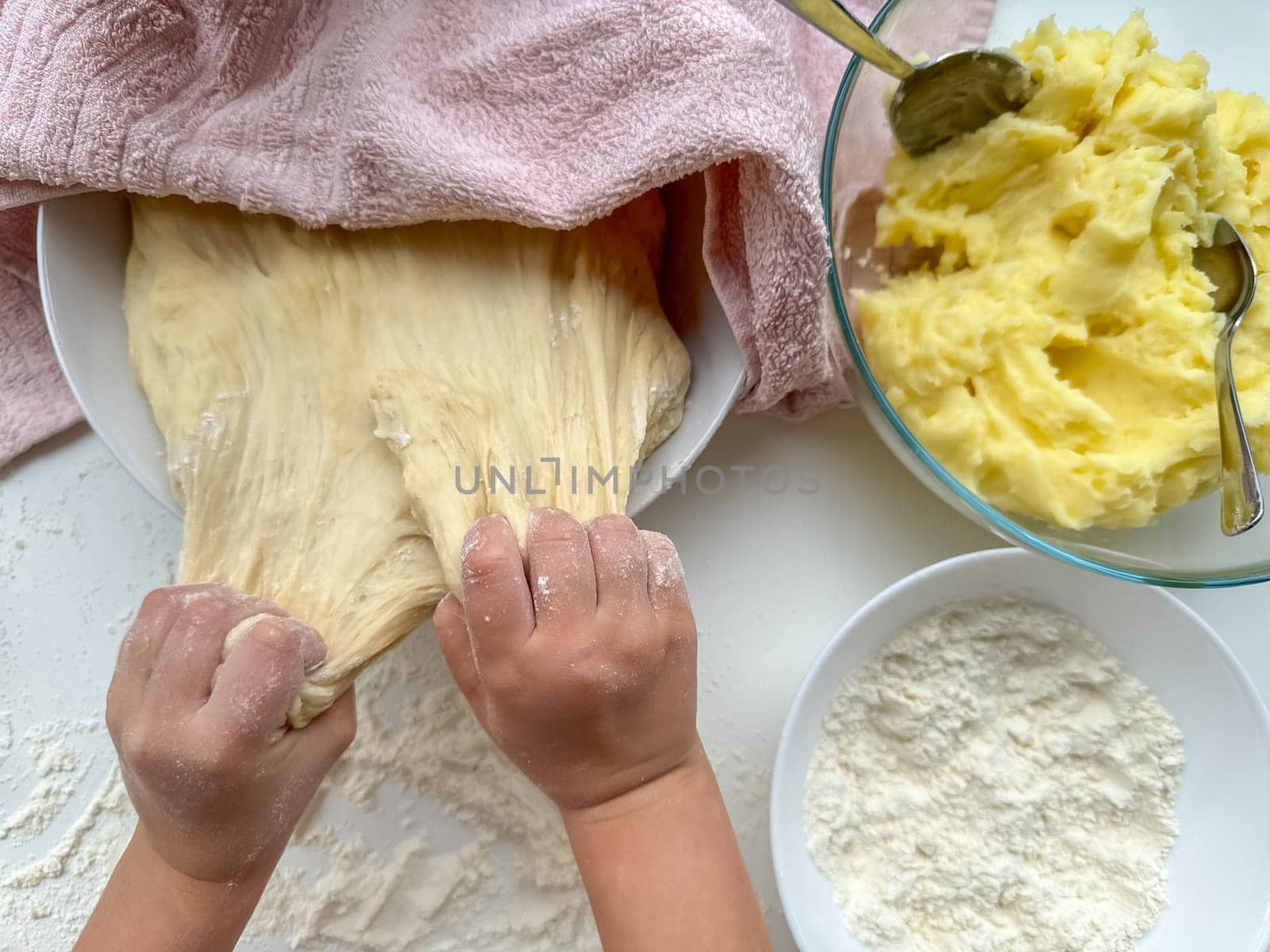 The hands of child knead the dough for making pies on white table, top view. High quality photo