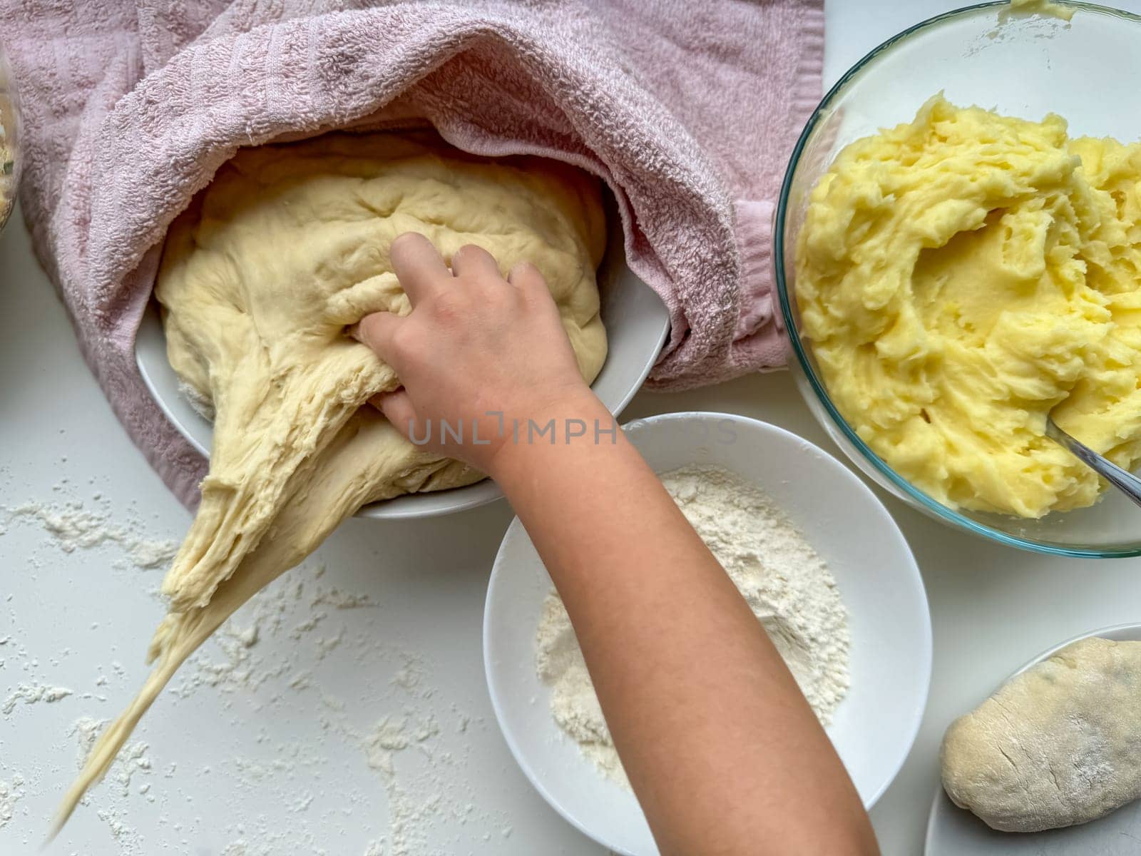 The hands of child knead the dough for making pies on white table, top view. High quality photo