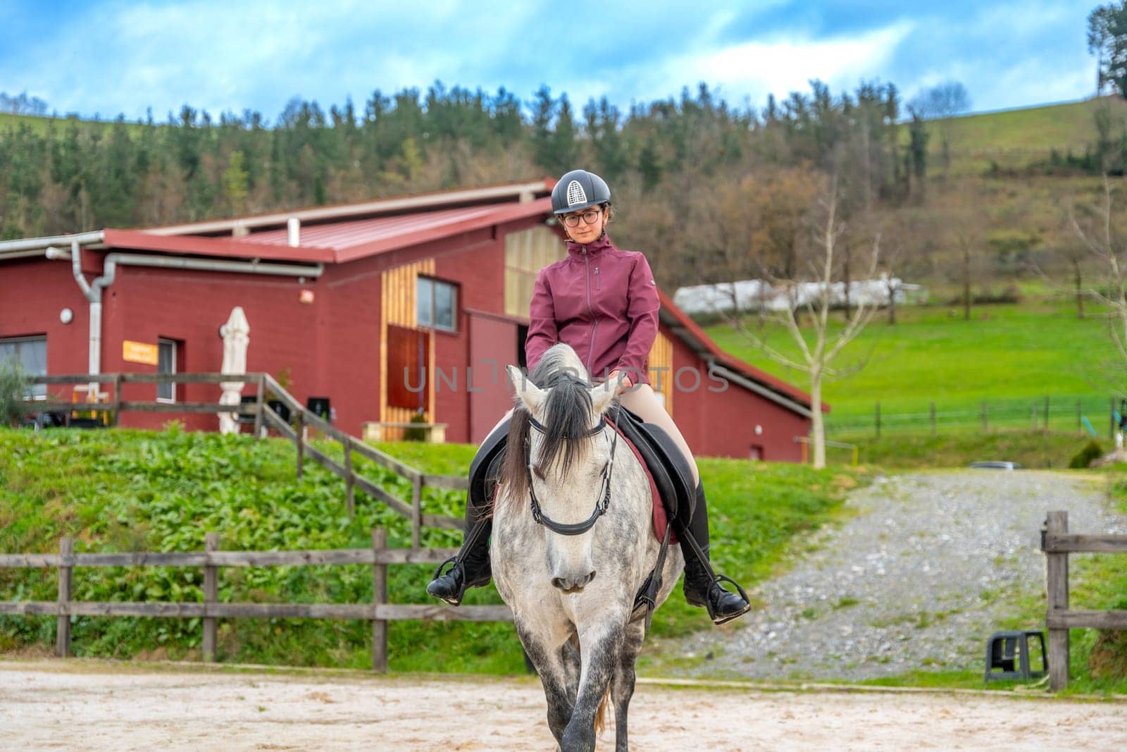 Frontal view of a young woman riding a white horse in a calm equestrian center