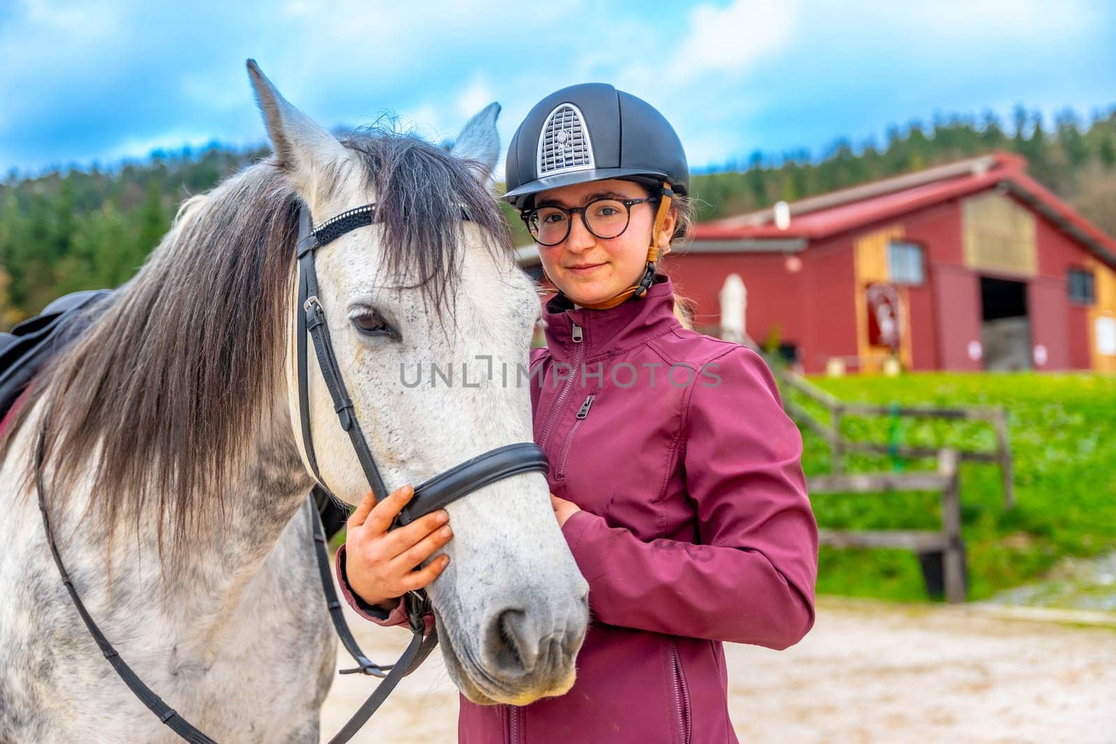 Outdoor portrait of a happy young girl with her white horse in an equestrian center