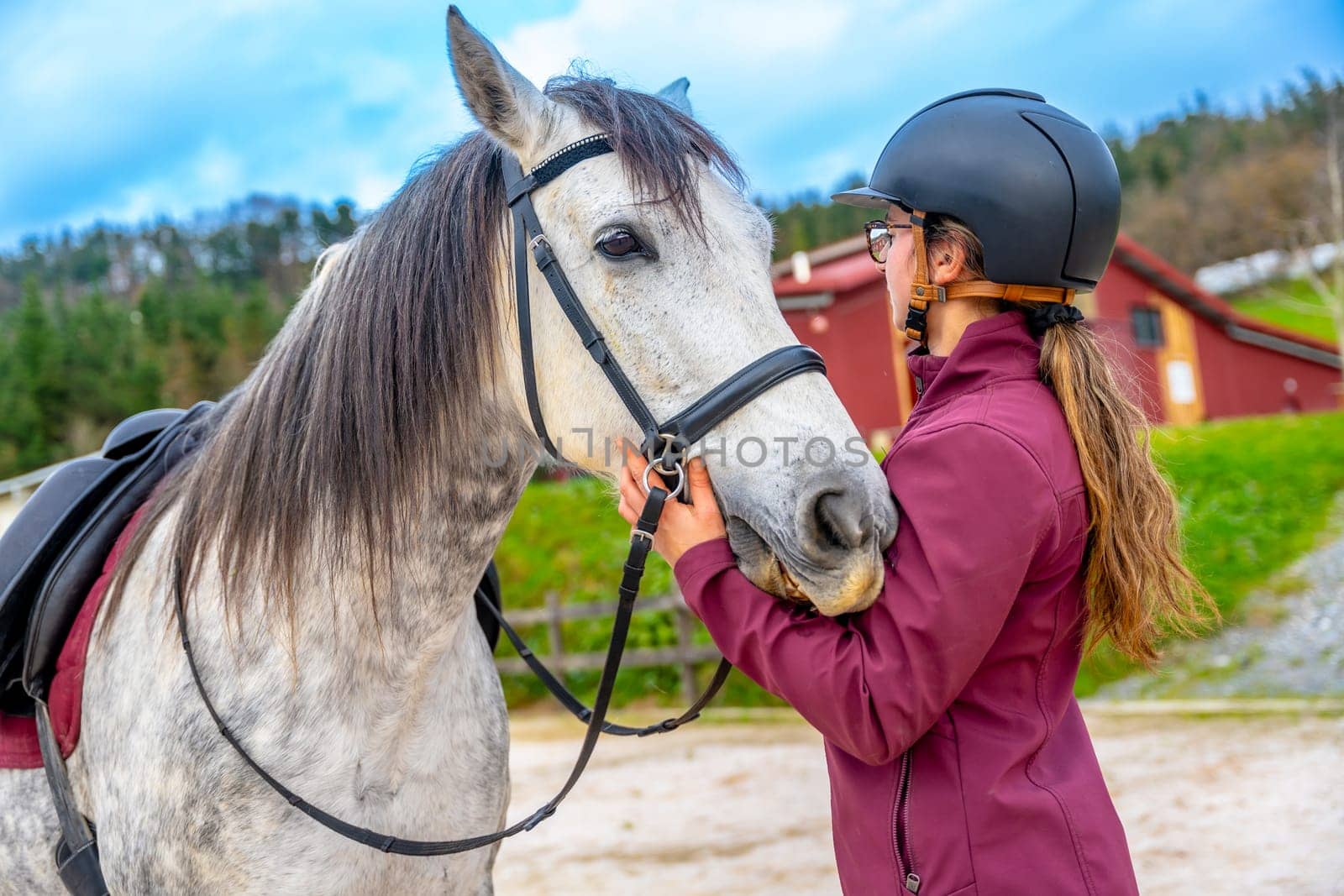 Woman with protective gear standing embracing her horse in equestrian center