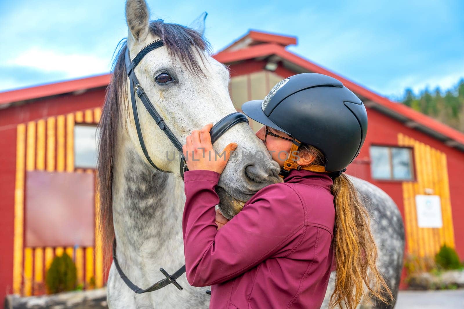 Woman with sport helmet kissing a horse outside an equestrian center
