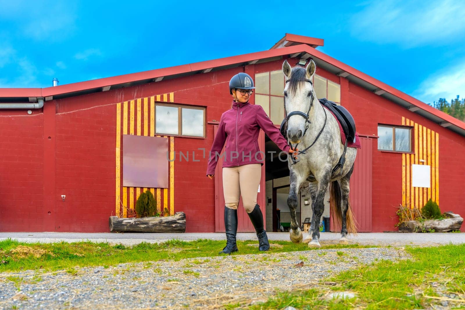 Wide view photo of a female young horse trainer and white horse walking along a rehabilitation center