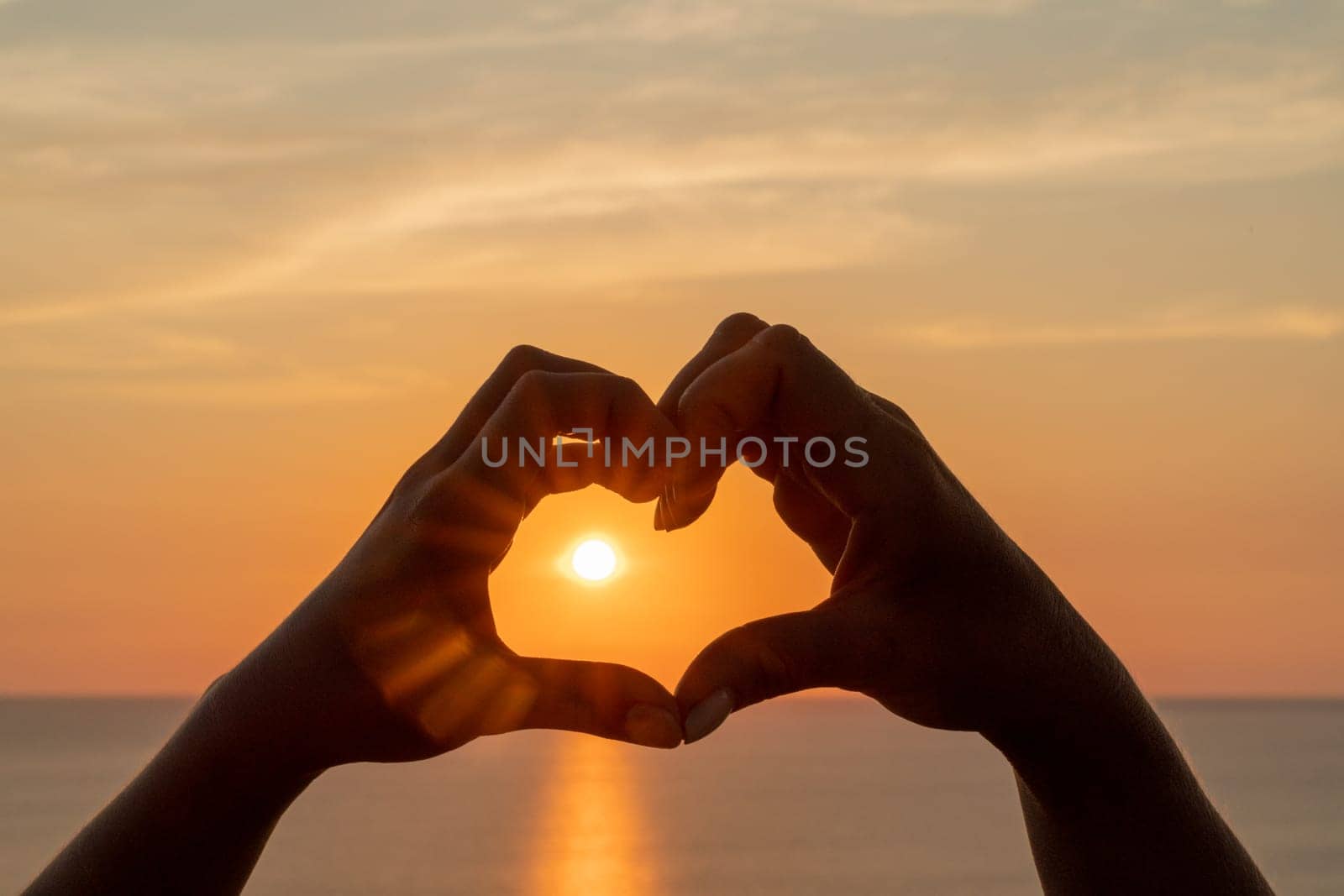 Hands heart sea sanset. Hands forming a heart shape made against the sun sky of a sunrise or sunset on a beach by Matiunina