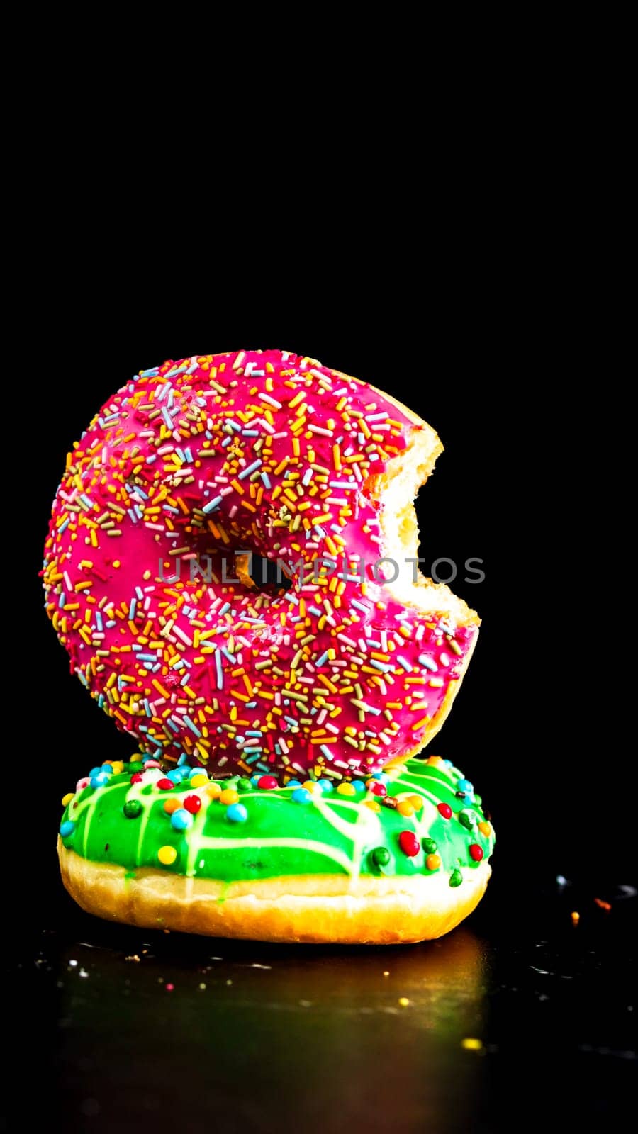 Bitten pink glazed donut with sprinkles isolated. Close up of colorful donuts.