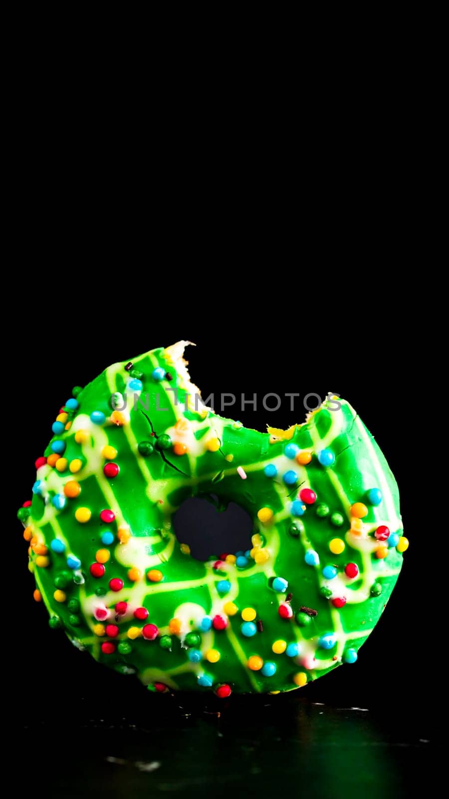 Green glazed donut with sprinkles isolated. Close up of colorful bitten donut.