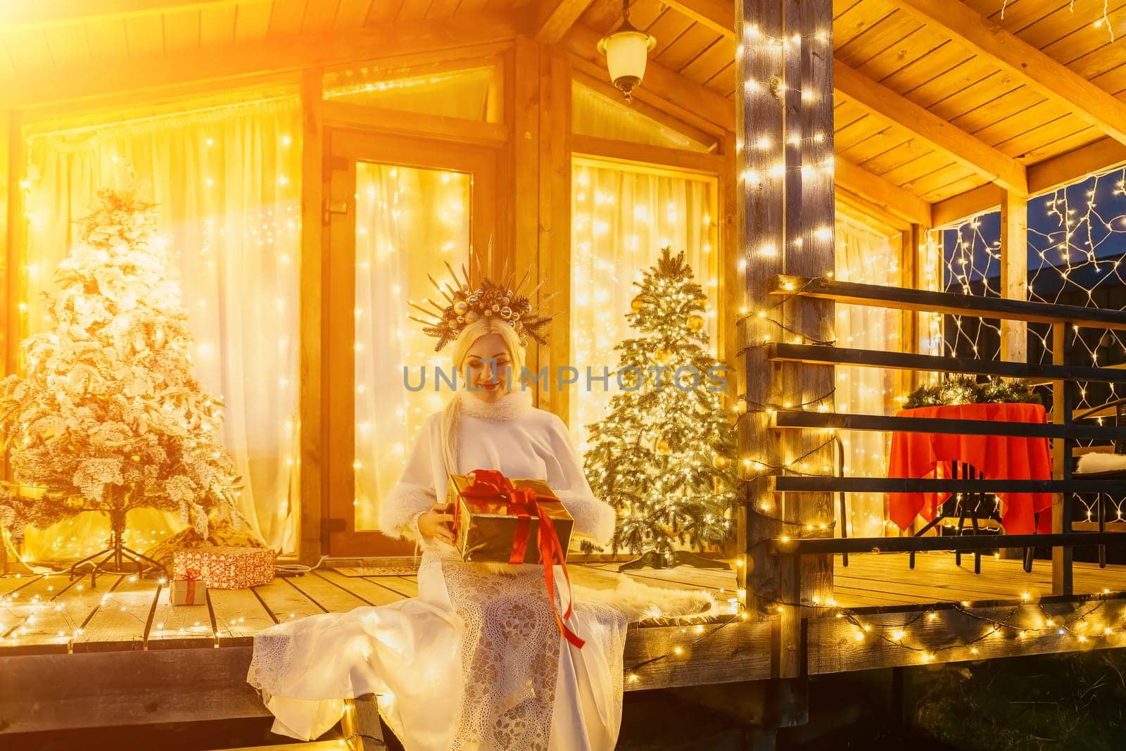 Happy smiling woman in a white dress holding a gift box in front of a Christmas tree. by panophotograph
