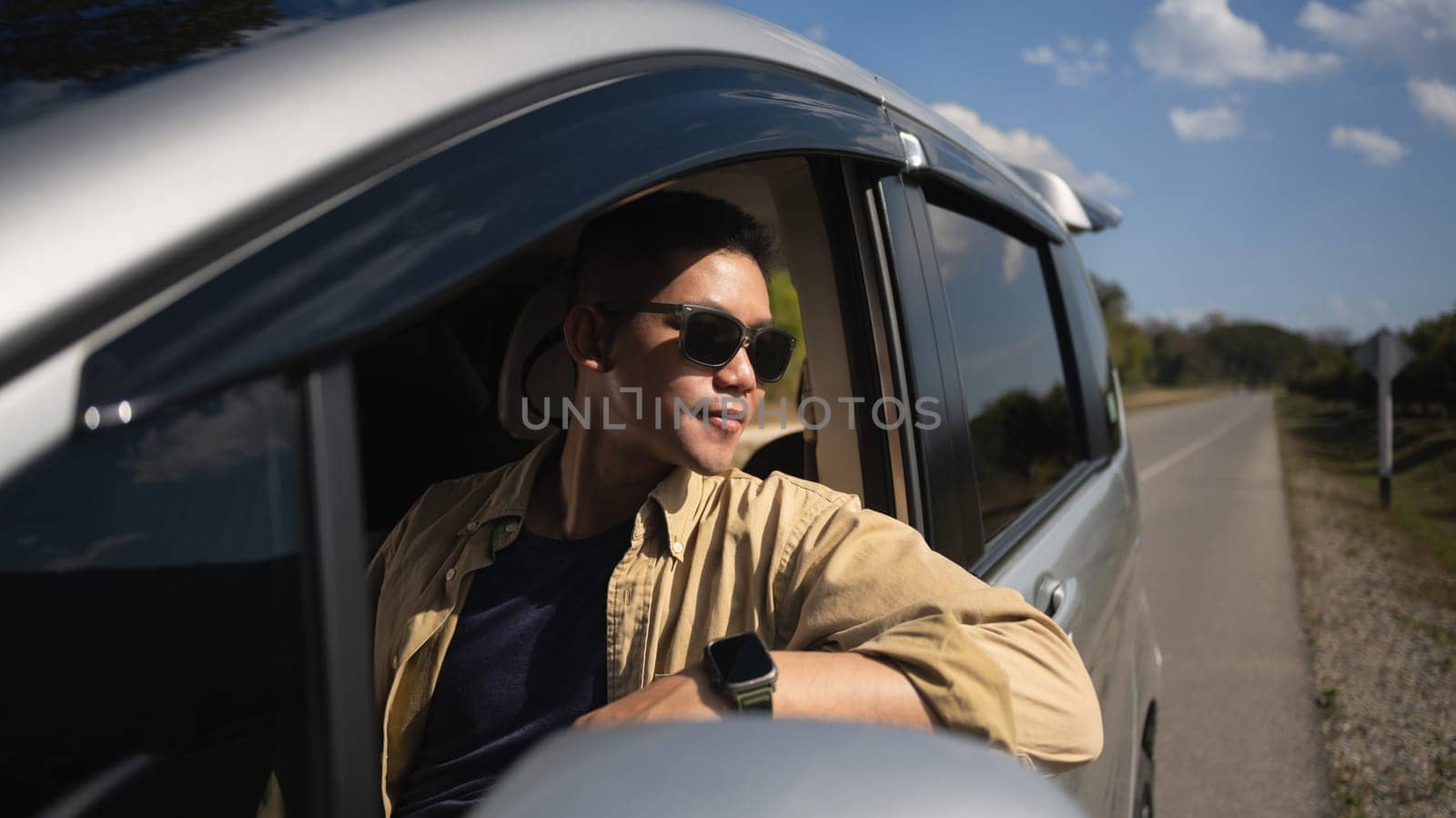 Attractive man in sunglasses driving car and enjoying nature views during summer roadtrip.