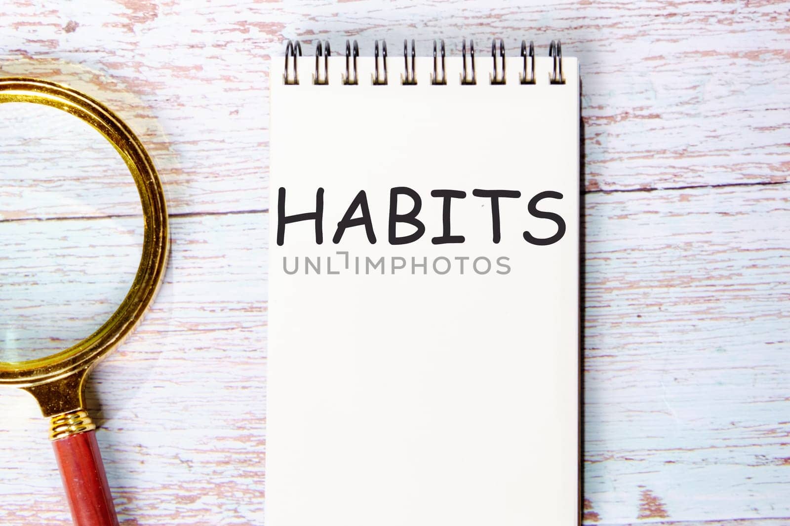 HABITS a word written on a notebook on wooden boards next to a magnifying glass