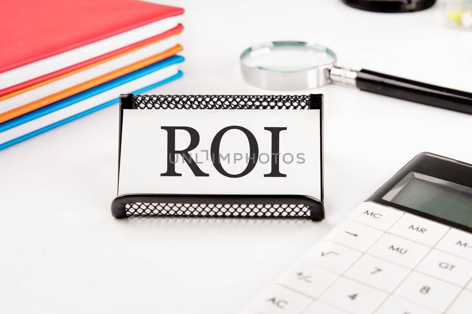 Return on investment concept. ROI text on a business card next to office supplies on a white background