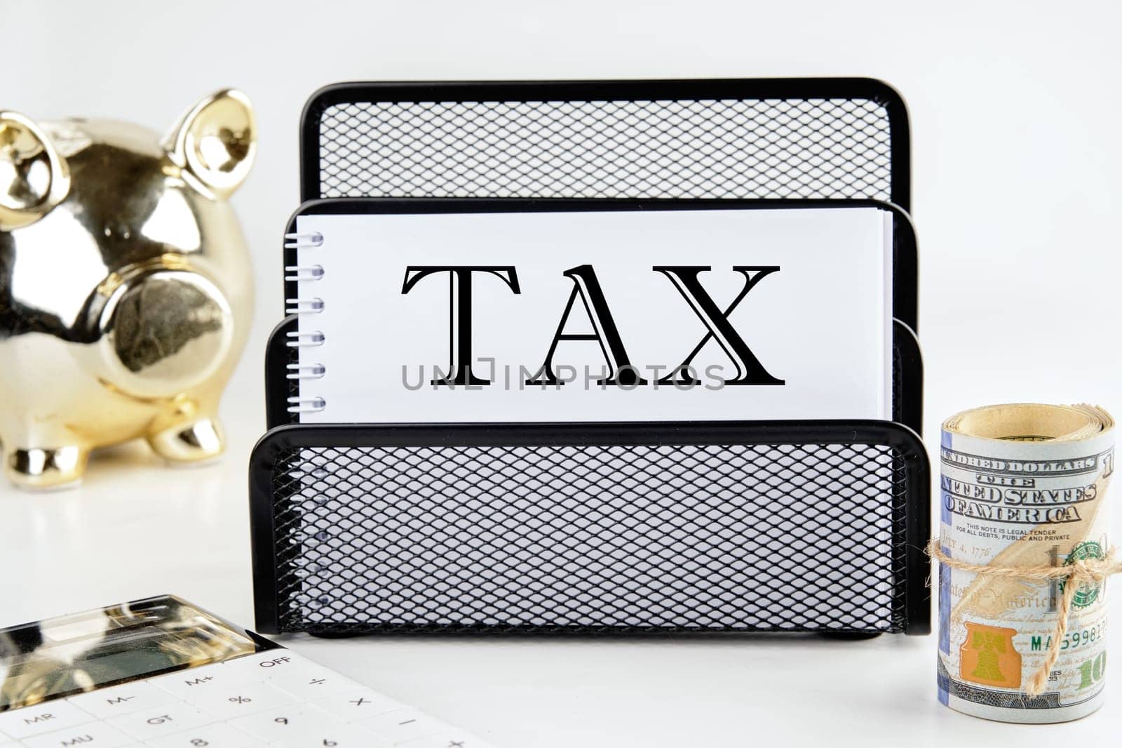 TAX text on a white piece of paper next to a piggy bank, a roll of money and a calculator on a white background