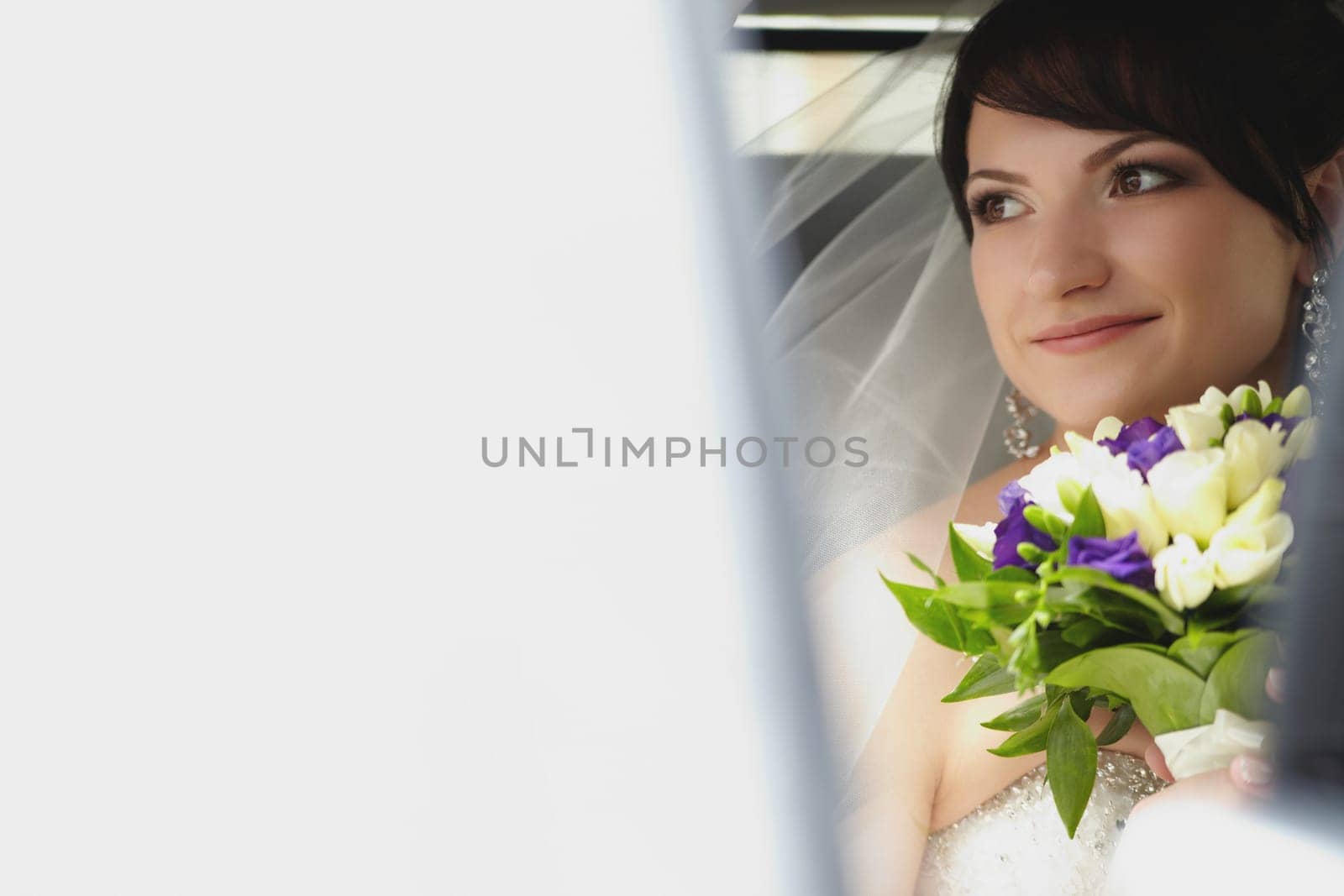 A young brunette bride is sitting in a car in close-up with a colorful bouquet of flowers on a summer day