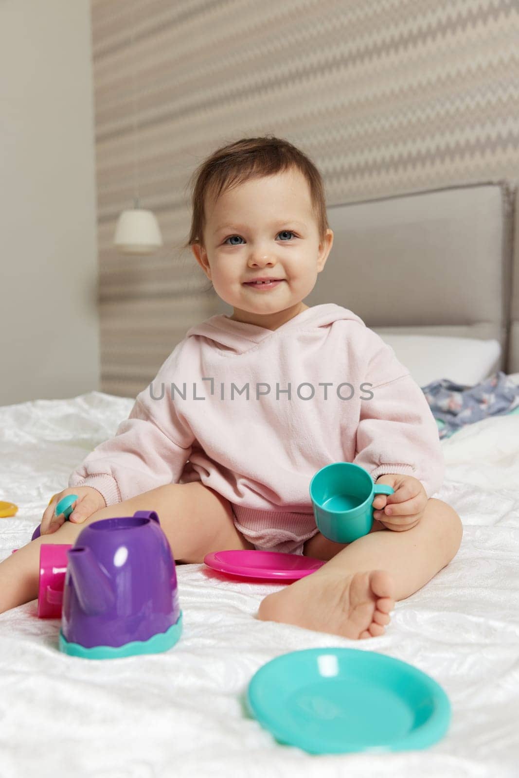 happy cute little child girl playing and pretending drinking tea from toy cups on bed