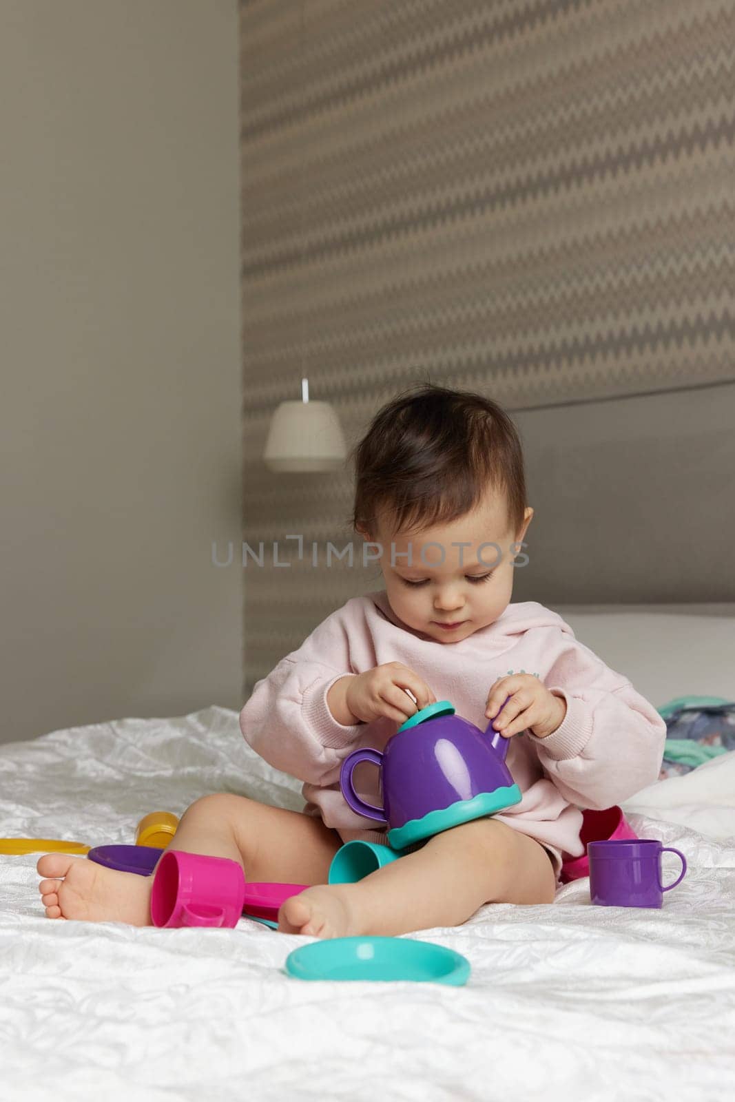 happy cute little child girl playing and pretending drinking tea from toy cups on bed
