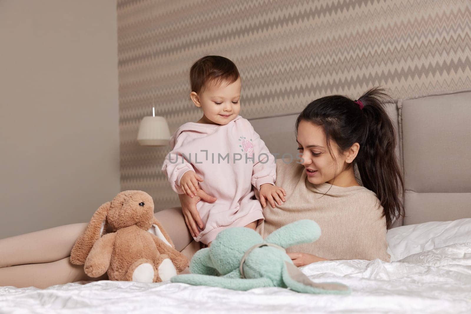 happy mother and her little child daughter playing with bunny toys in bedroom, family having fun