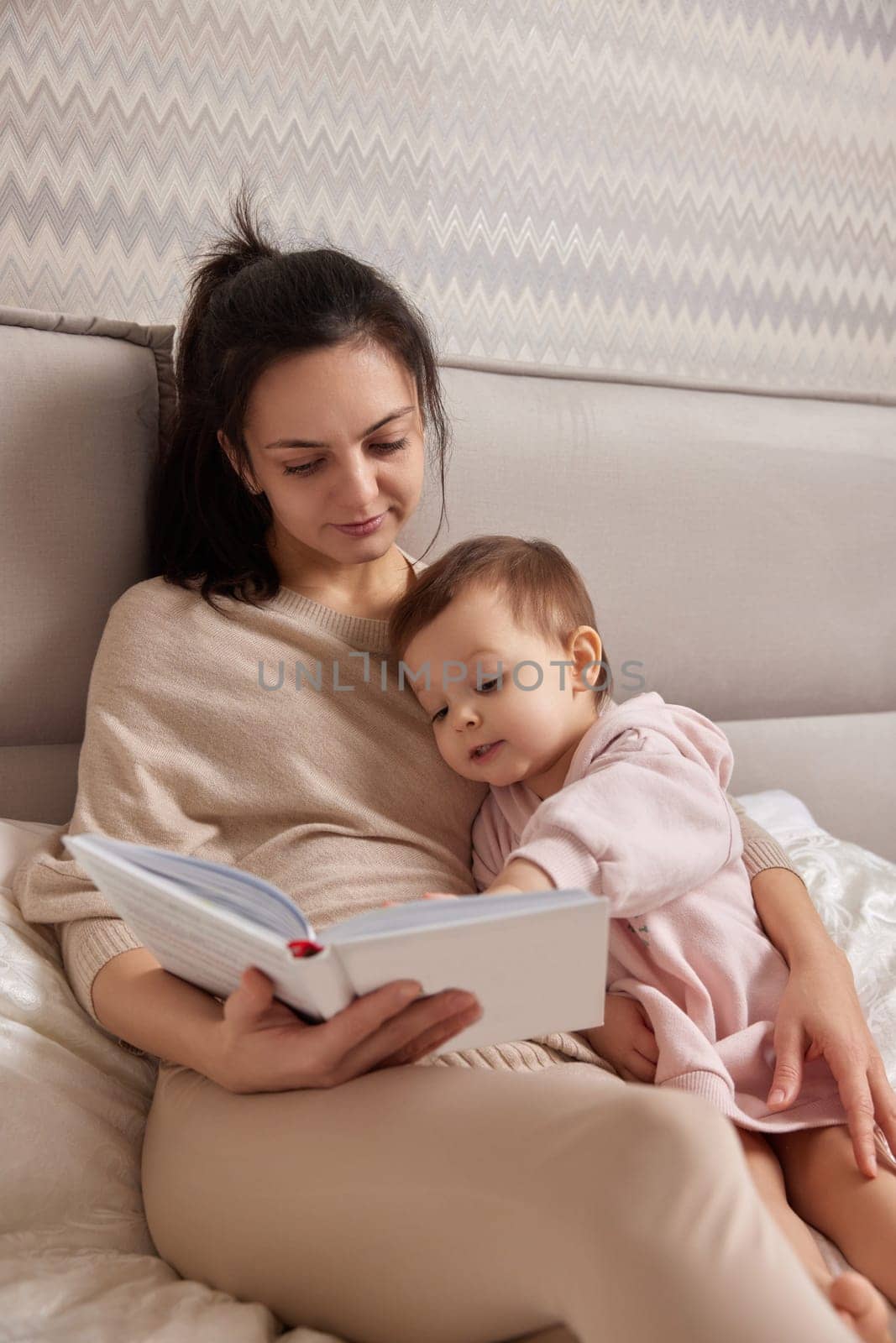 beautiful mother reading book to her cute little daughter on bed