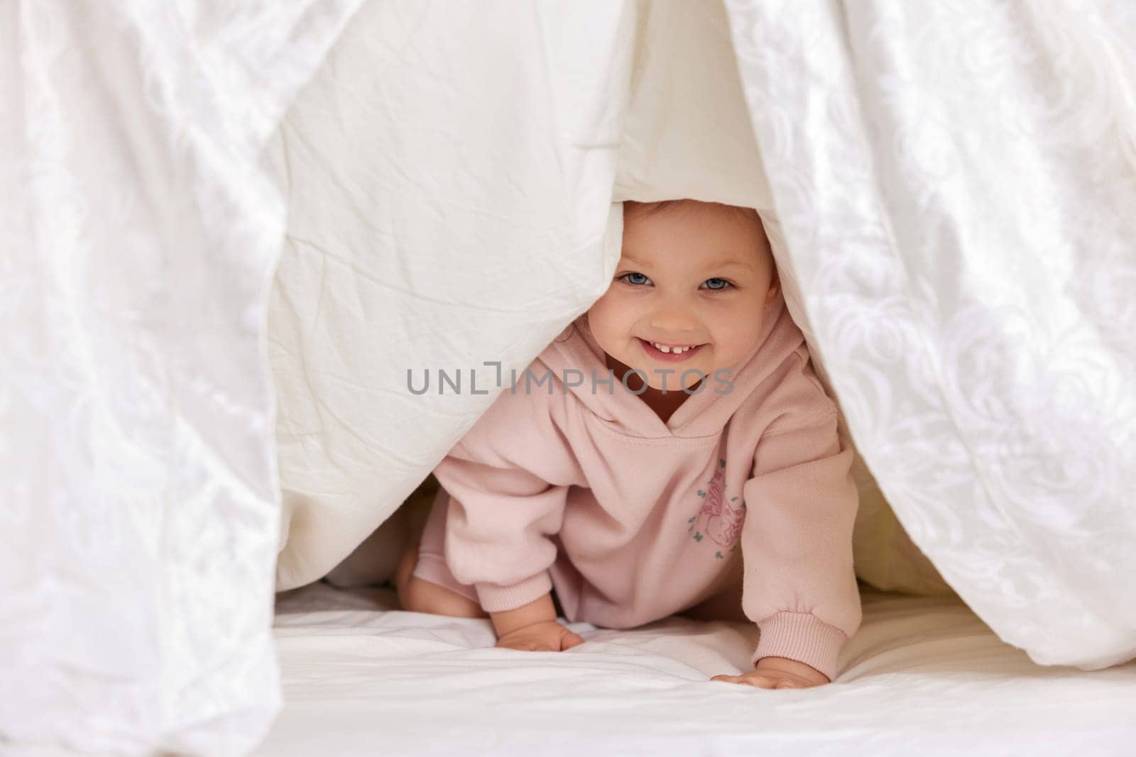 cute funny little child girl looks out from under the blanket on the bed, copy space
