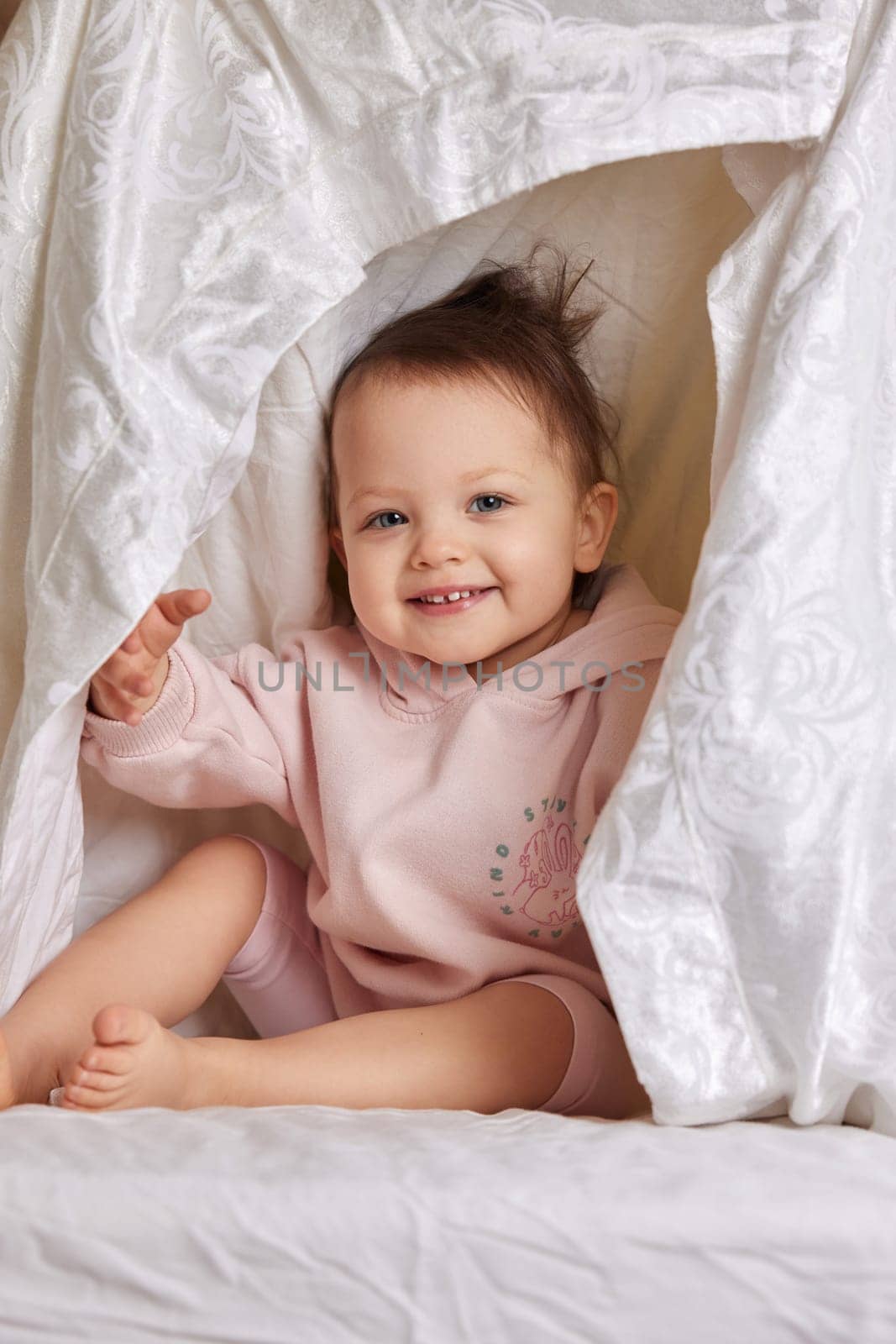 cute funny baby girl hiding under blanket on the bed