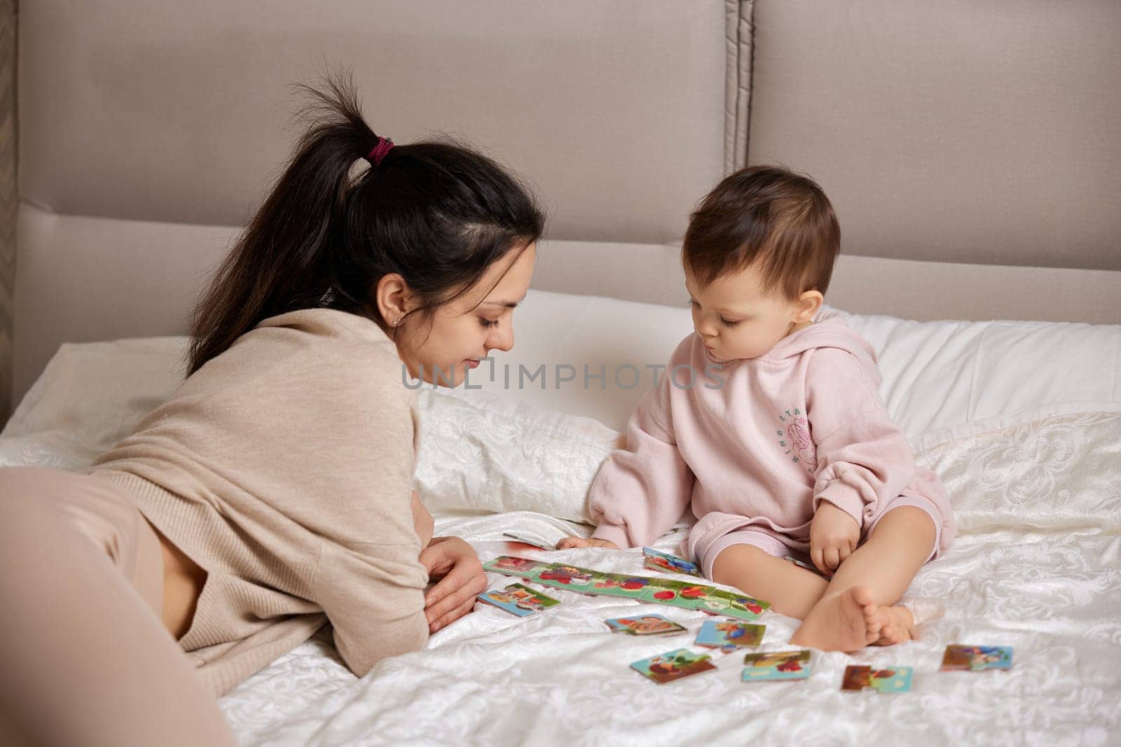 beautiful mother playing playing with puzzle pieces with little child girl in bedroom
