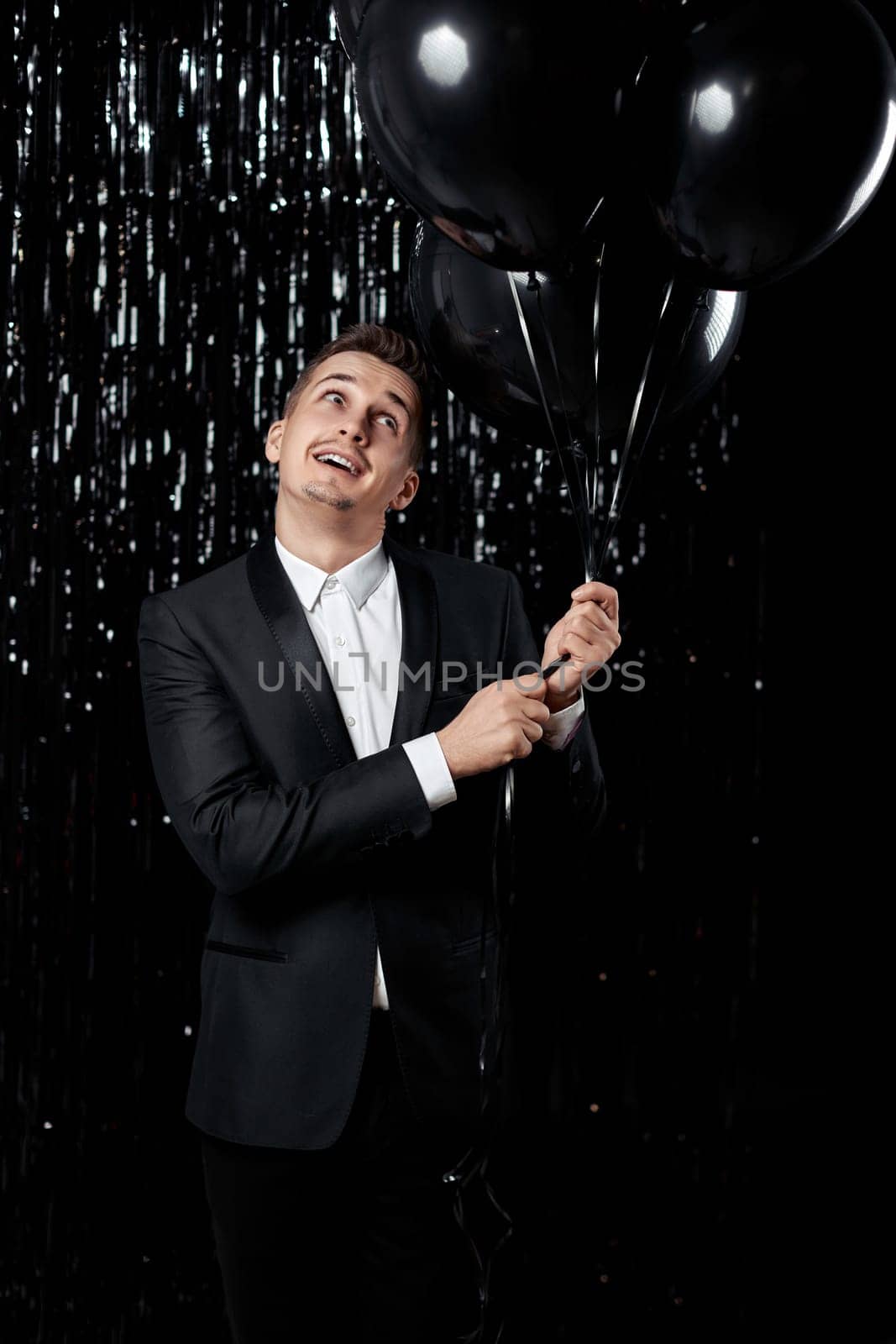 Happy handsome man in black jacket holding black air balloons on glitter background.