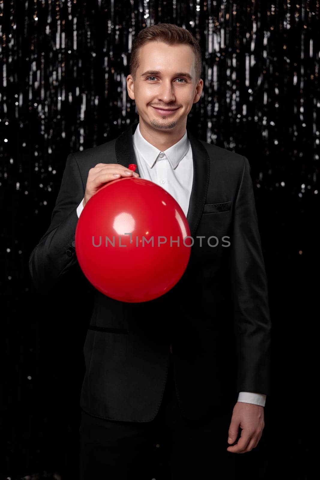 caucasian man in black jacket with red air balloon on dark glitter background. birthday party