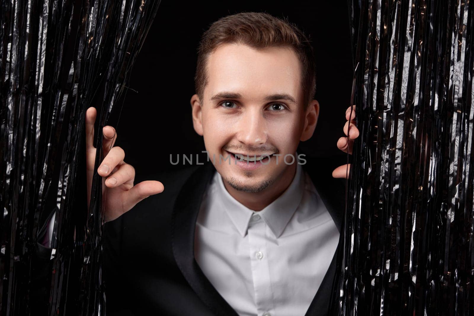 Happy handsome man in black jacket smiling on glitter background.