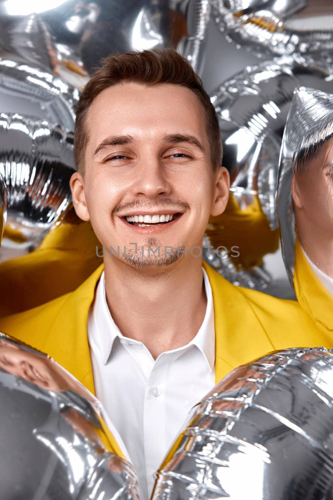 portrait of happy man in yellow jacket with a lot of silver air balloons. birthday party