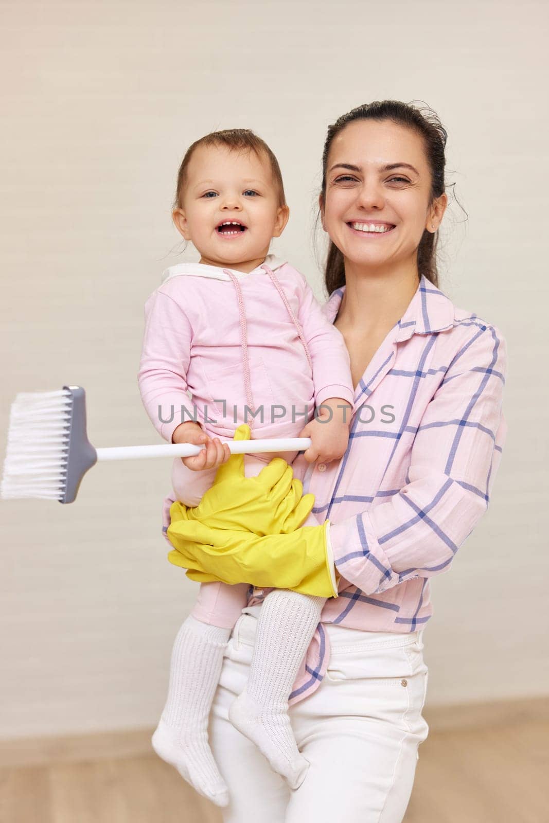 happy mother housewife is holding cute baby girl and doing housework at home , Happy family having fun