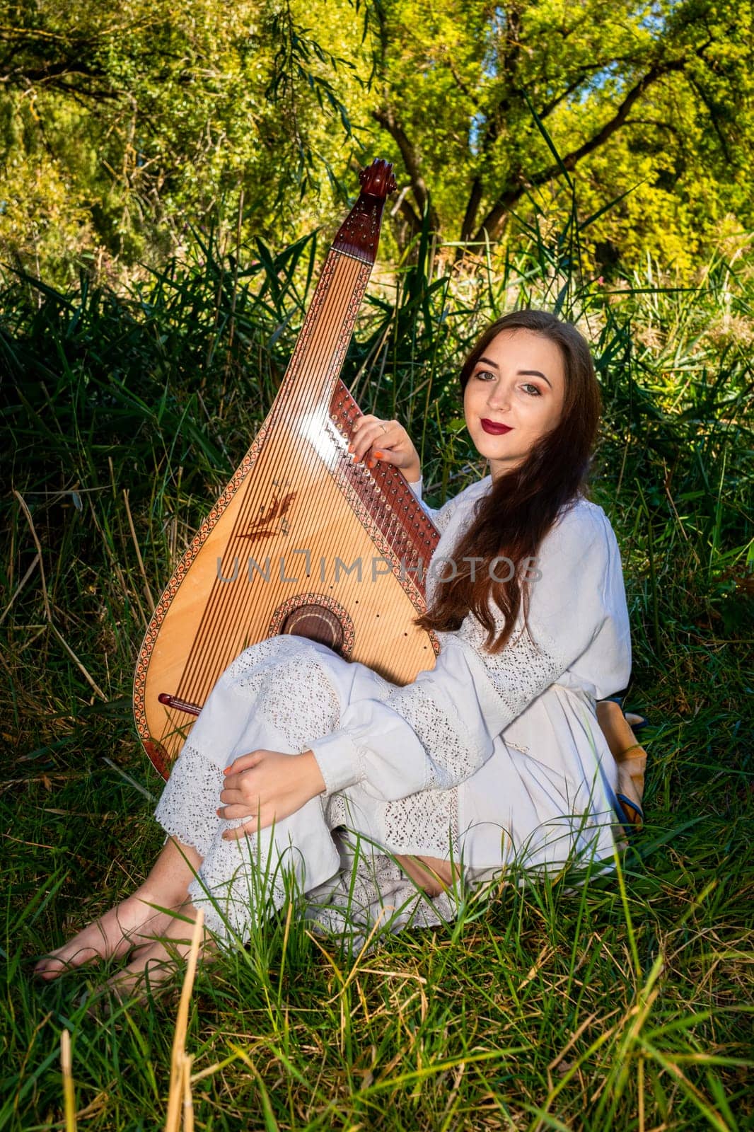 A girl with a musical instrument sits on the grass.