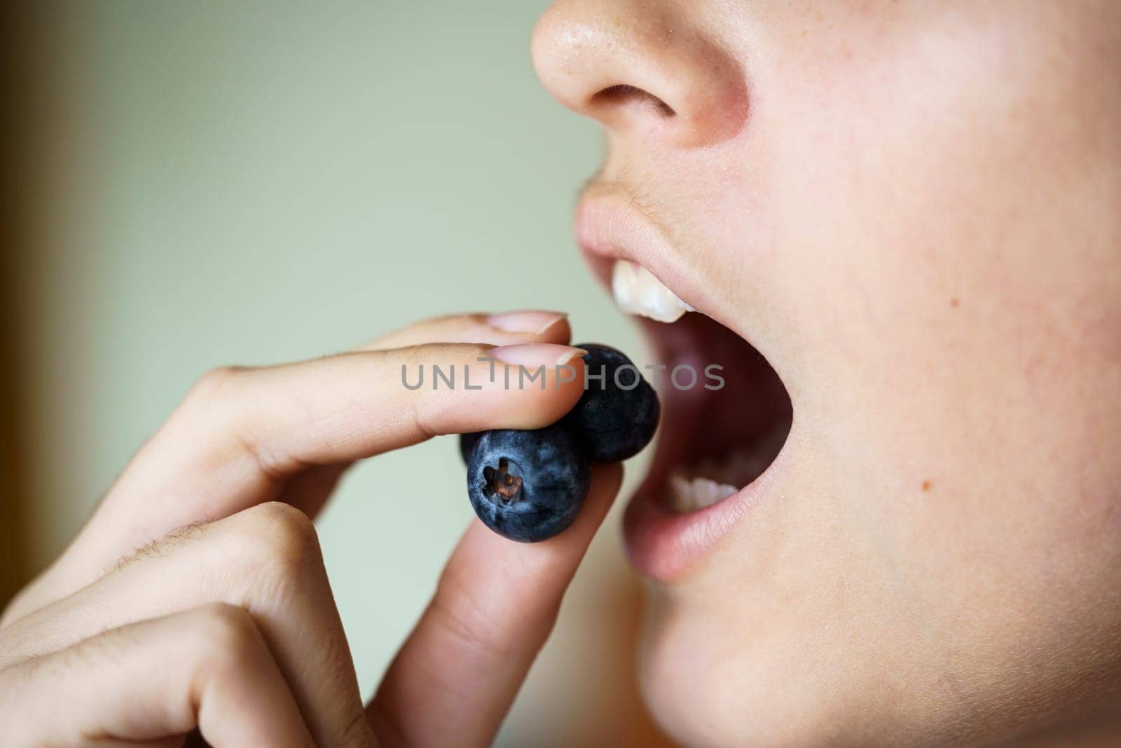 Closeup of crop anonymous young girl with mouth open about to eat delicious blueberries at home