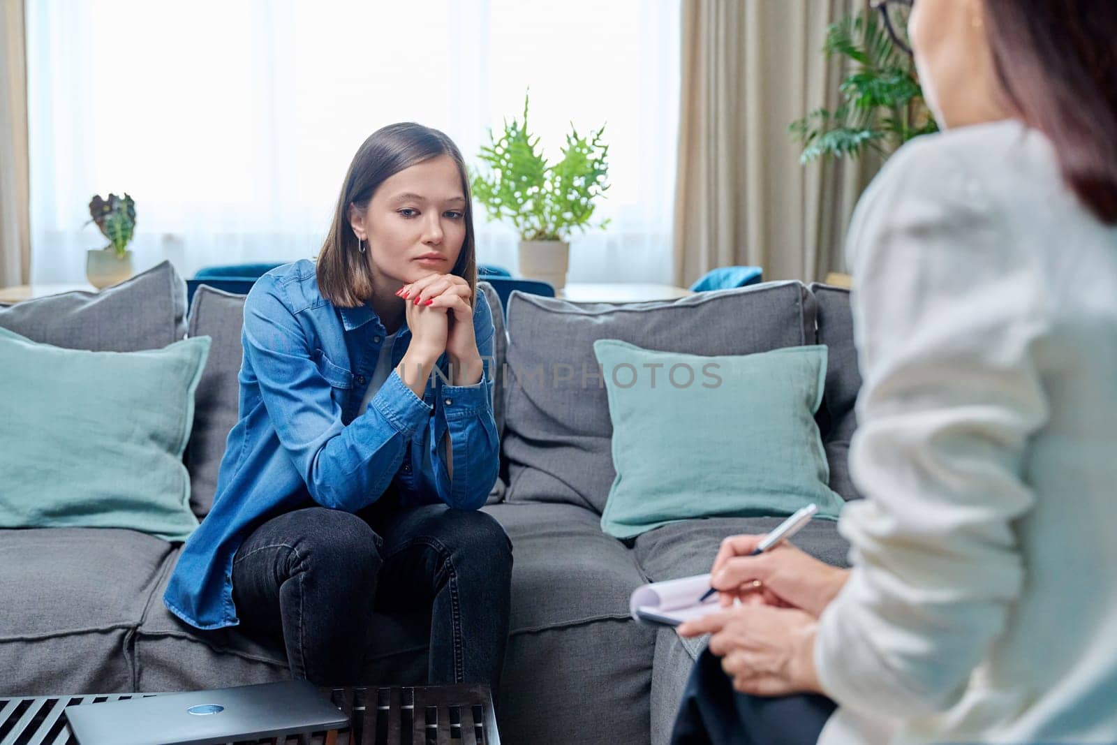 Sad young woman at therapy session with psychologist, psychiatrist. Therapist counselor and unhappy female patient on sofa in office. Psychology counseling treatment psychotherapy mental health youth