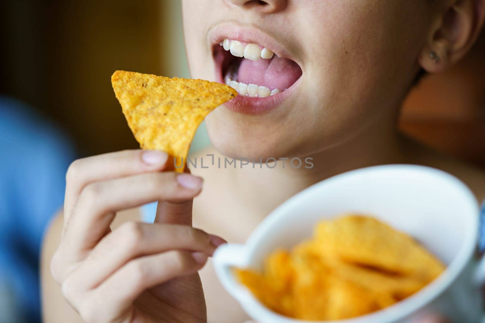 Crop unrecognizable teenage girl with mouth wide open about to eat spicy tortilla chip at home