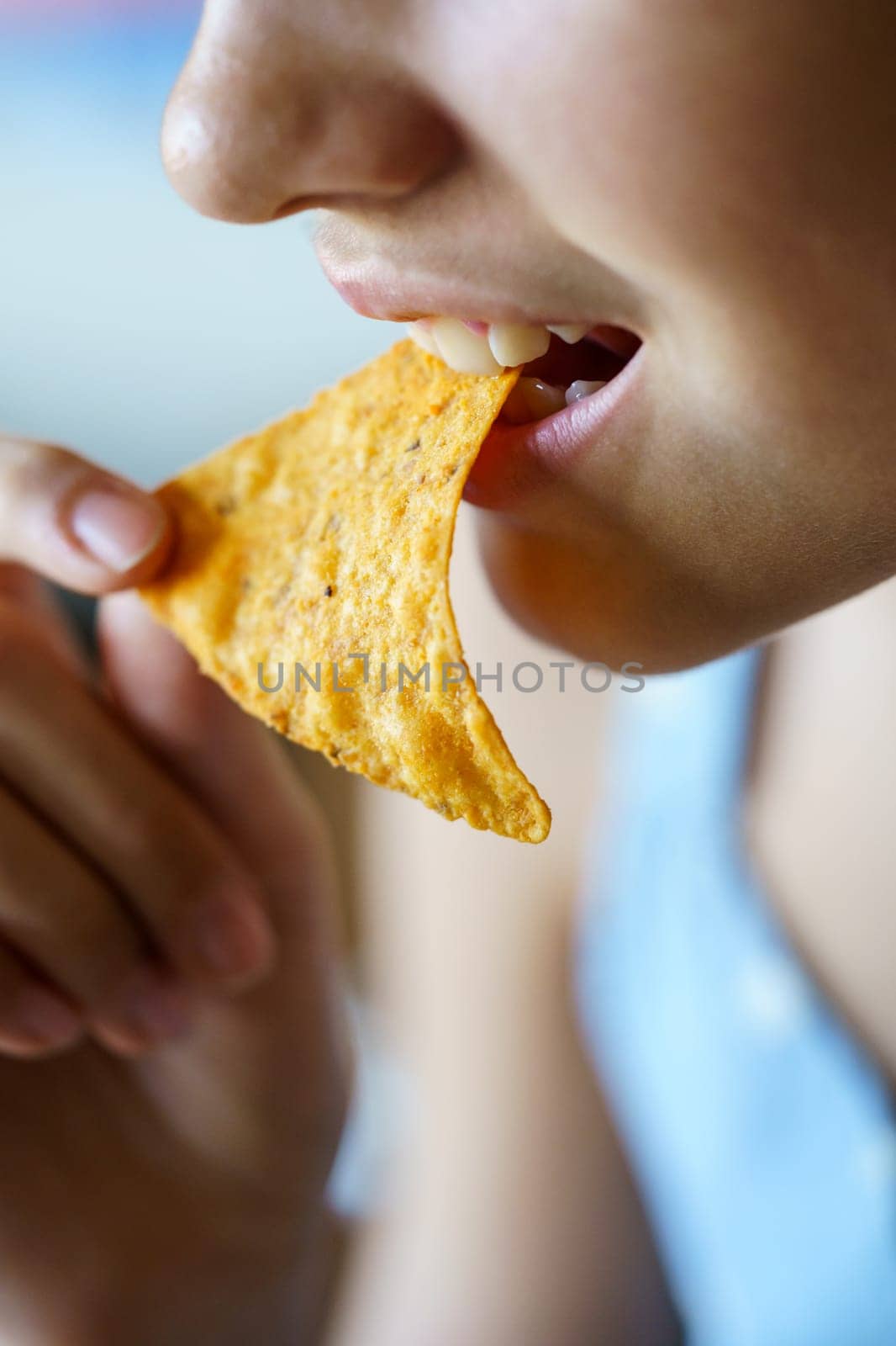 Closeup of crop anonymous teenage girl eating crunchy Mexican tortilla chip at home