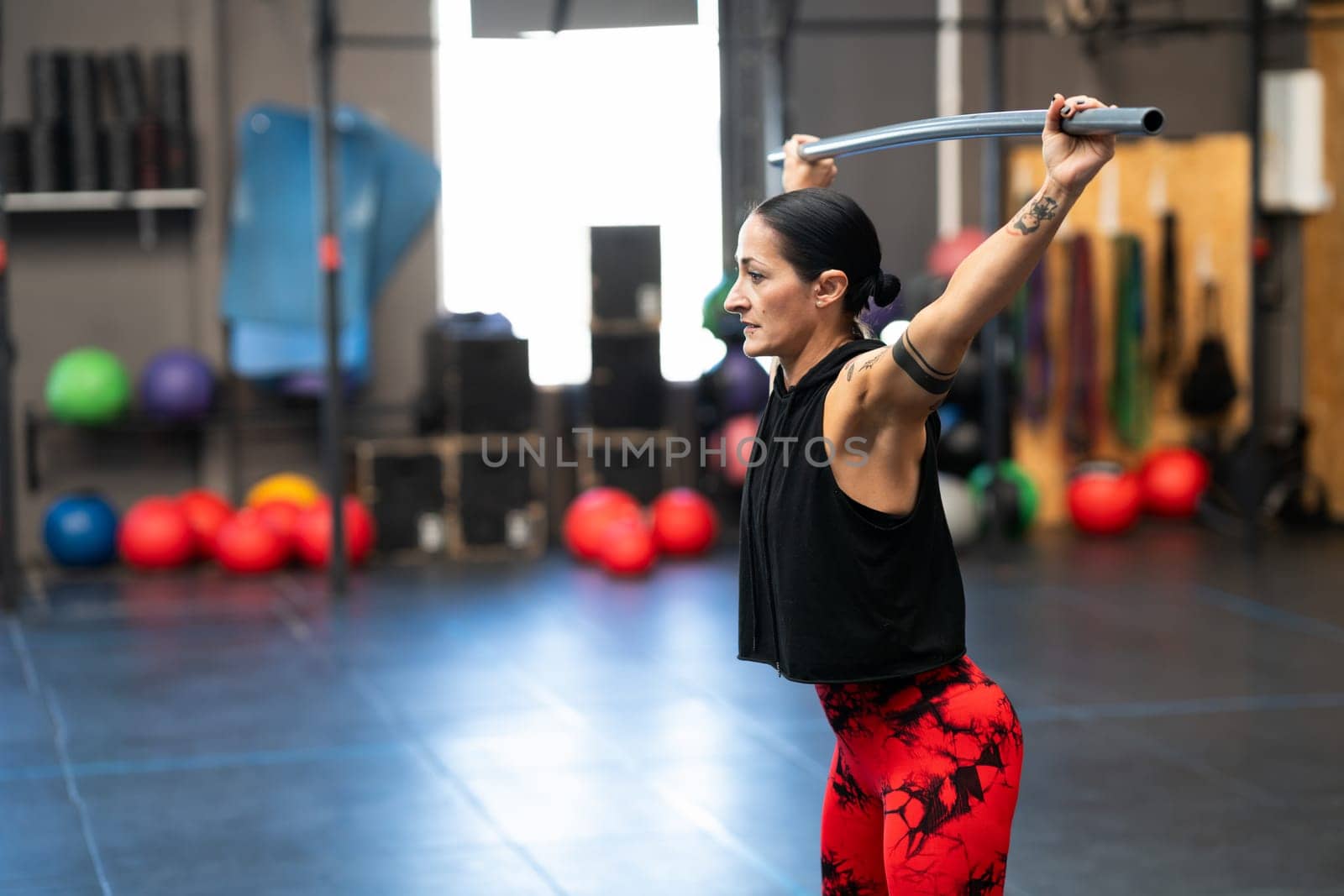Horizontal photo with copy space of a mature woman warming up and stretching with a bar in a cross training gym