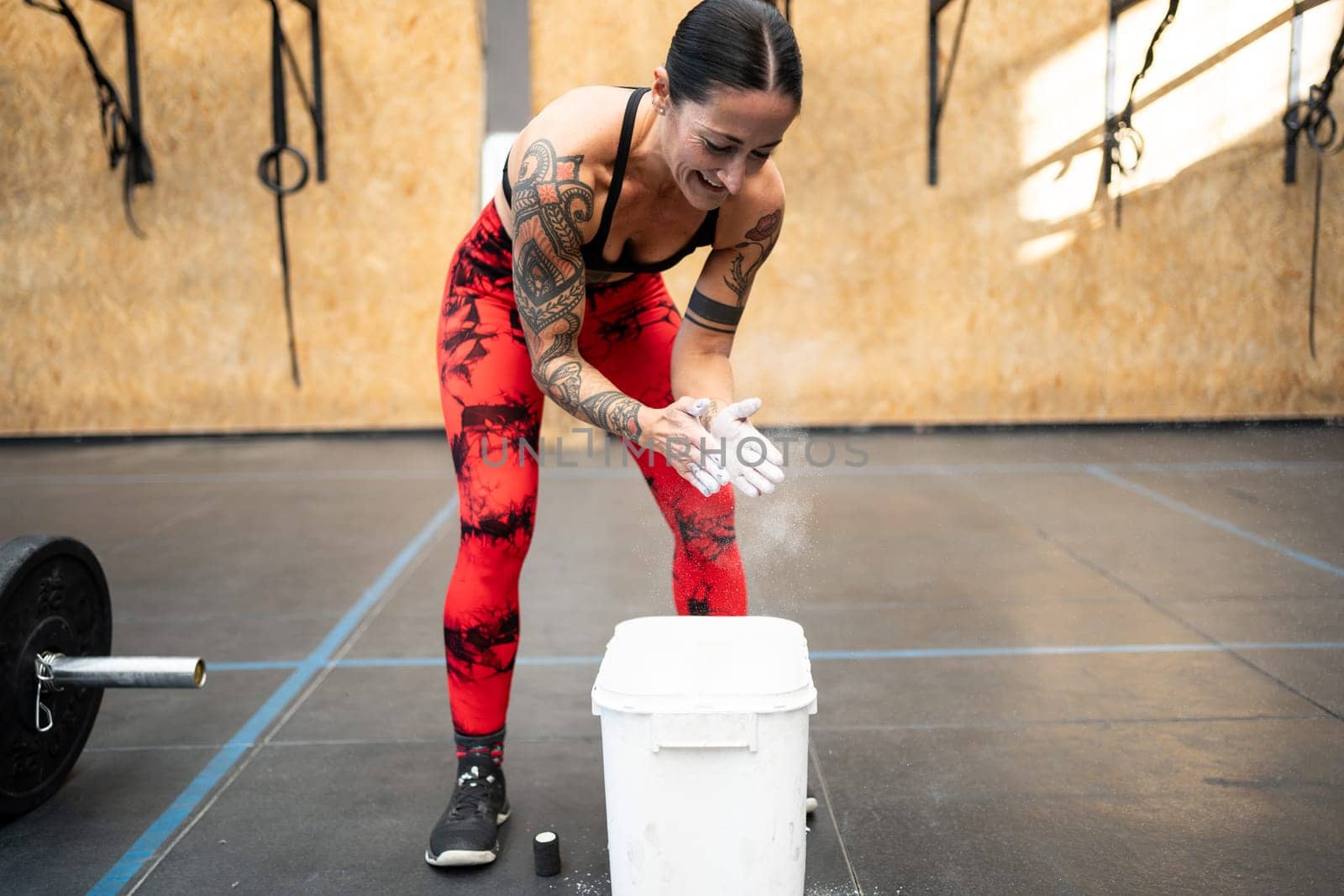 Mature fit woman with tattooed arms applying magnesium powder to her hands for weightlifting