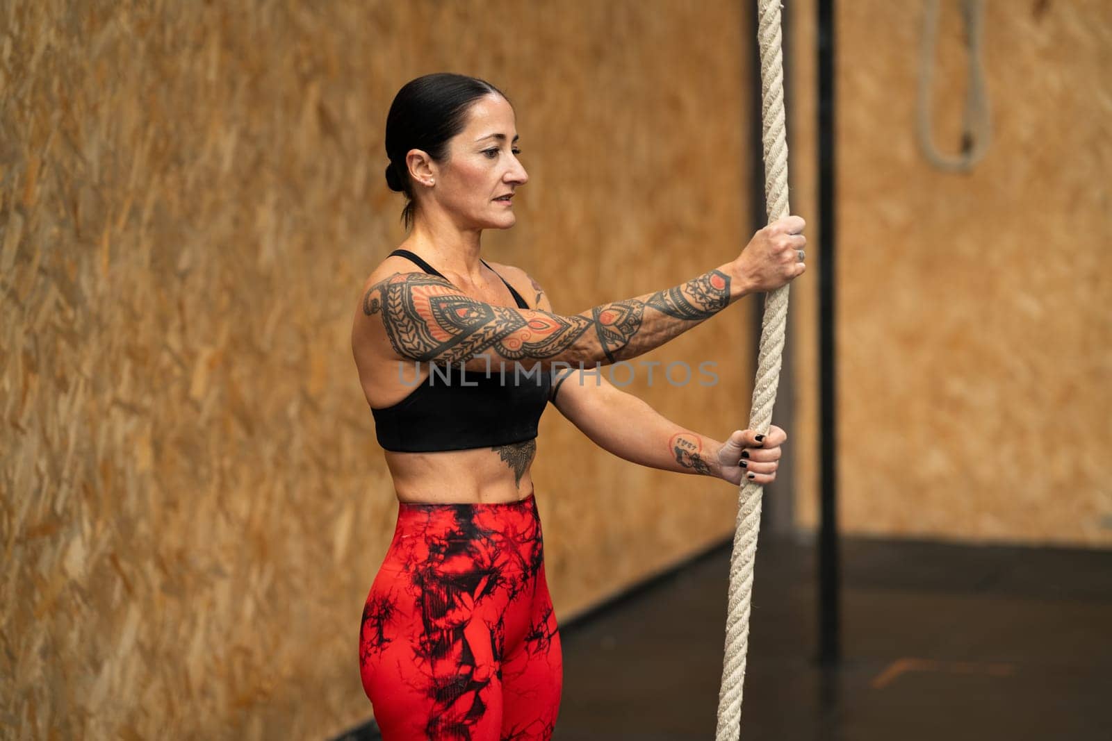 Mature strong woman about to start to climb a rope in a gym