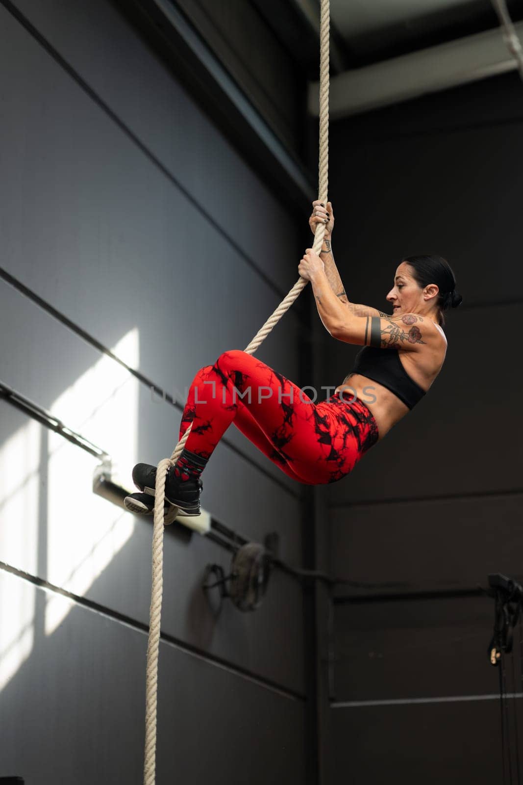 Strong woman climbing a rope in a cross training gym by javiindy