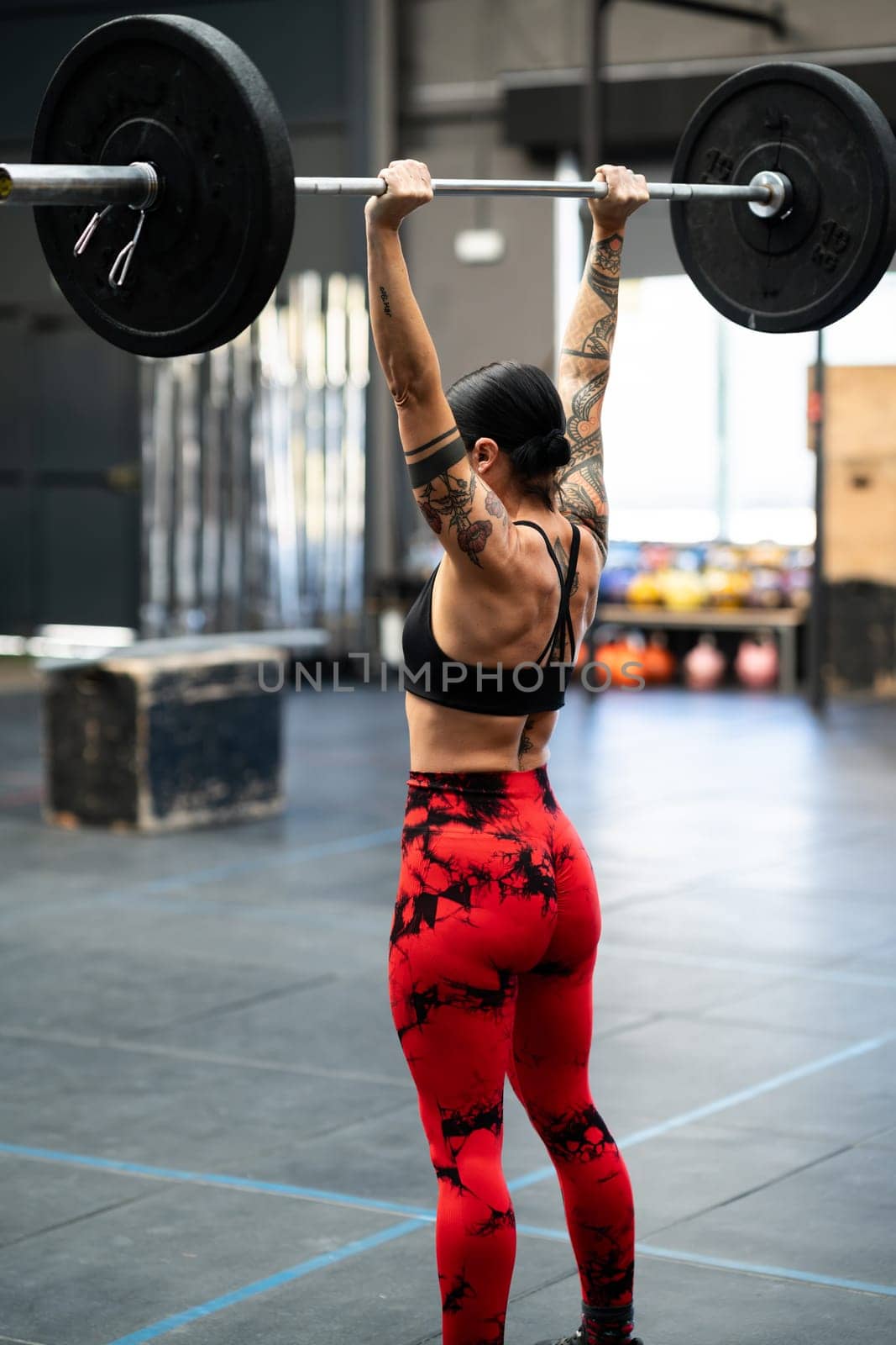 Vertical rear view of a mature sportive and strong woman bodybuilding in a gym