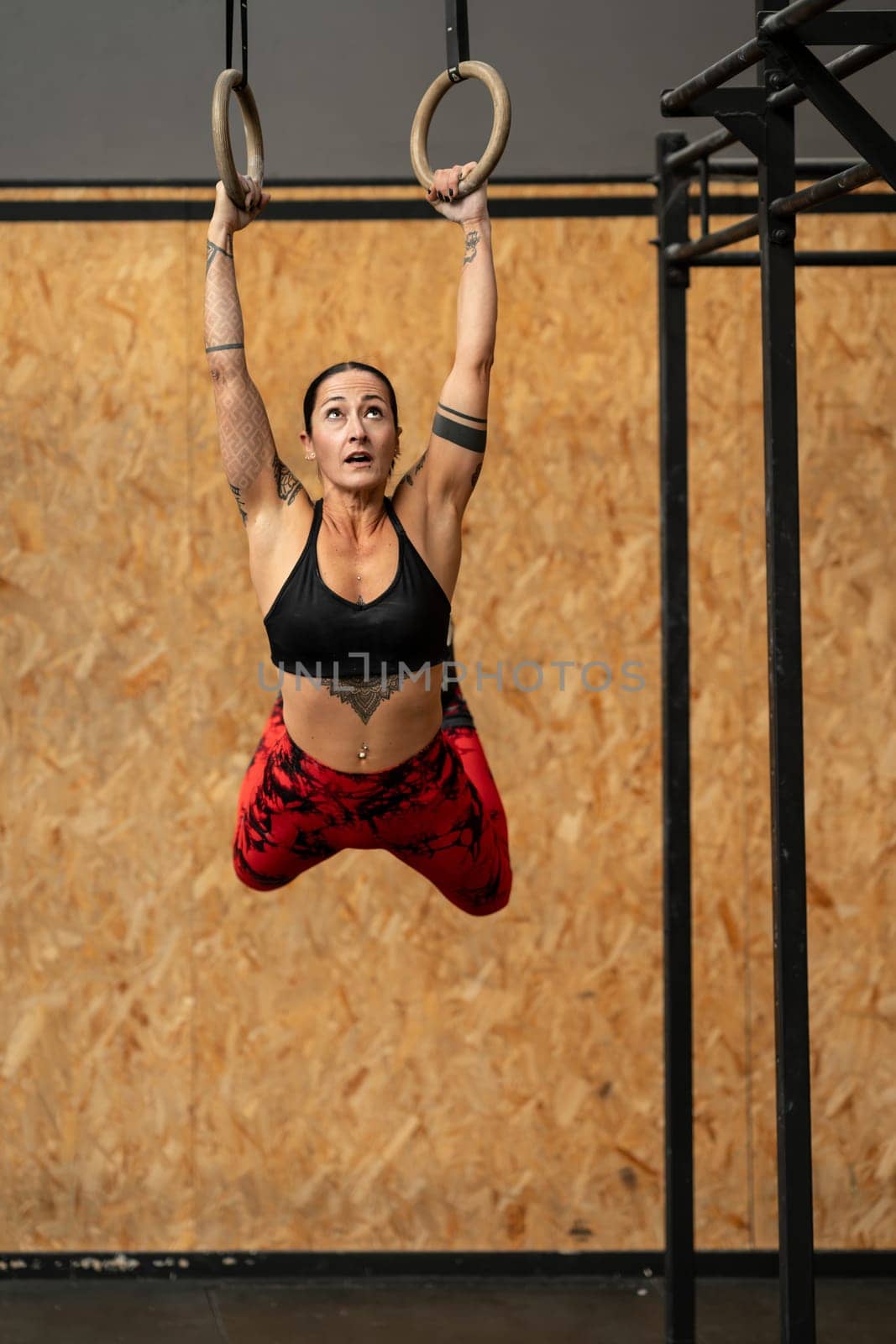 Sportive woman hanging from olympic rings while working out by javiindy