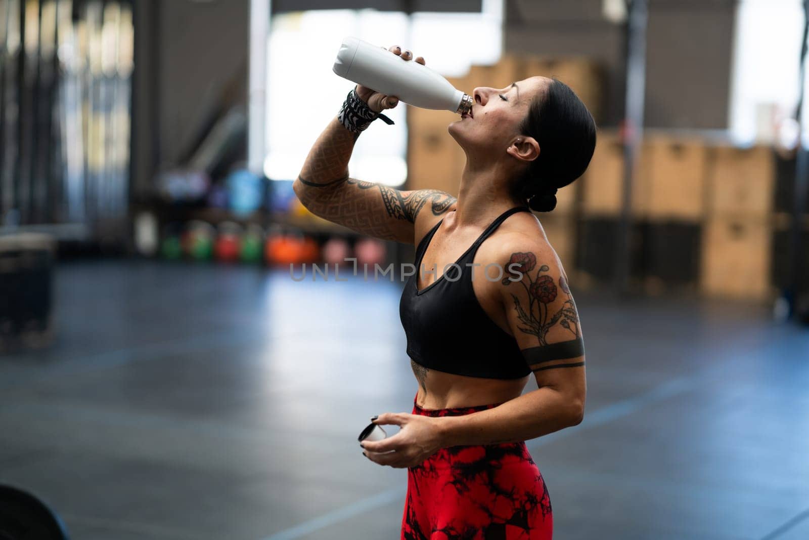 Side view of a fit woman drinking water form a reusable bottle in a gym
