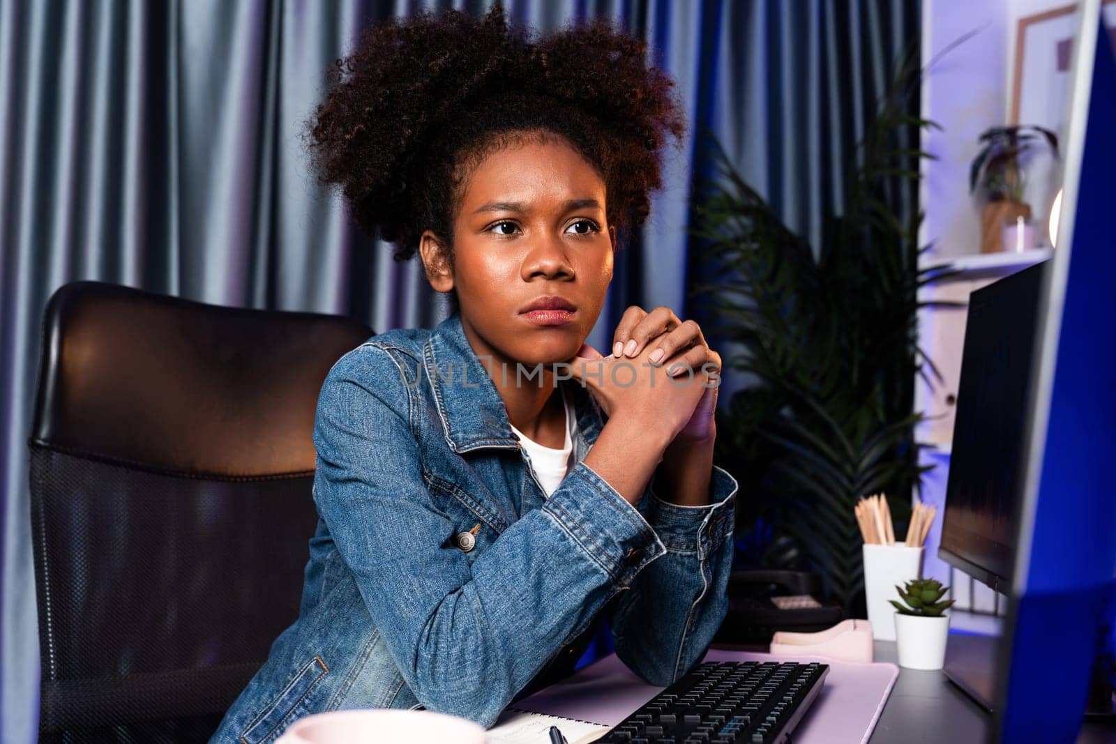 Young African creator looking on screen monitor laptop, wearing jeans shirt. Thinking the project or study new technology at workplace. Concept of job planing professional at home office. Tastemaker.